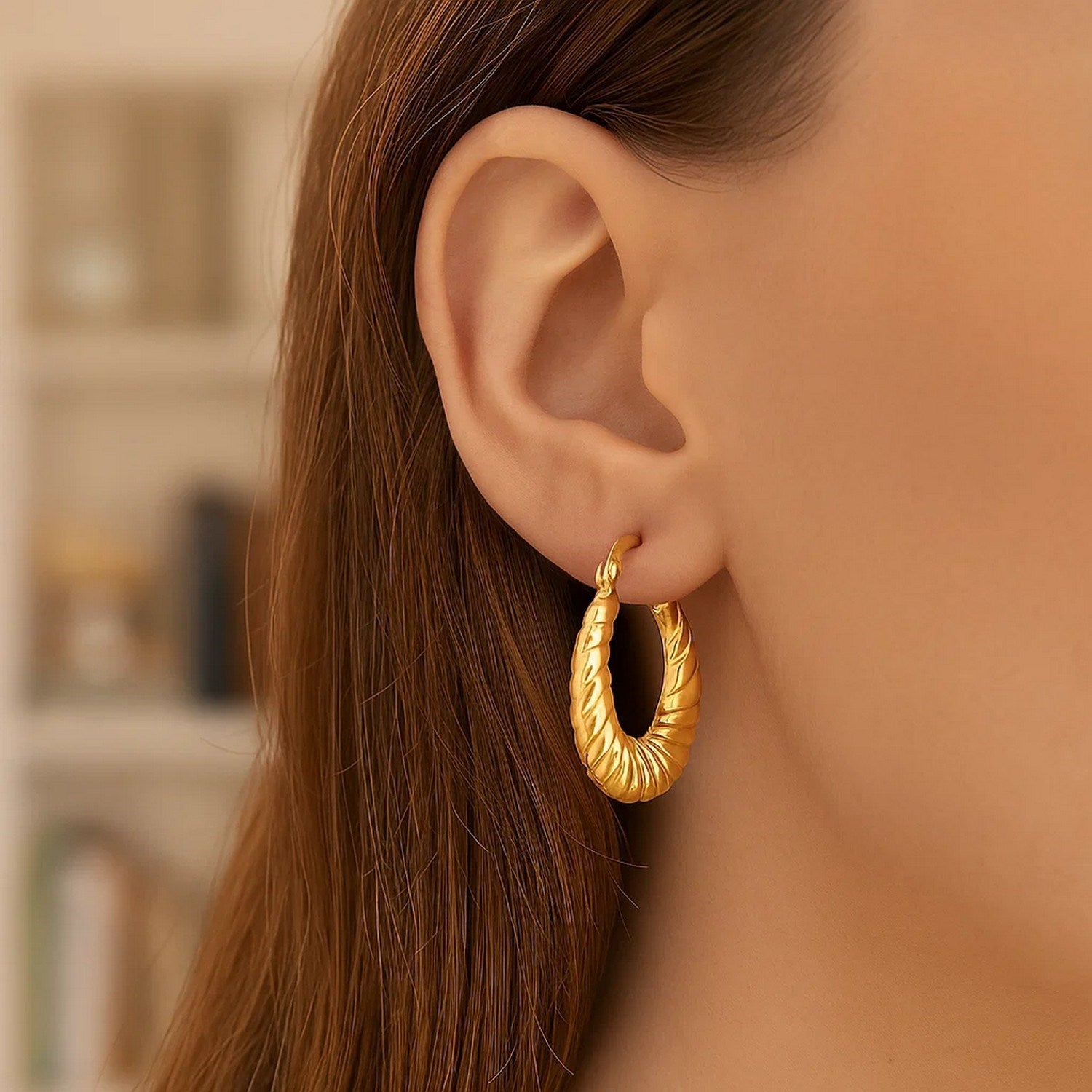 14K yellow gold polished twisted cable graduated hoop earring on a woman's ear.