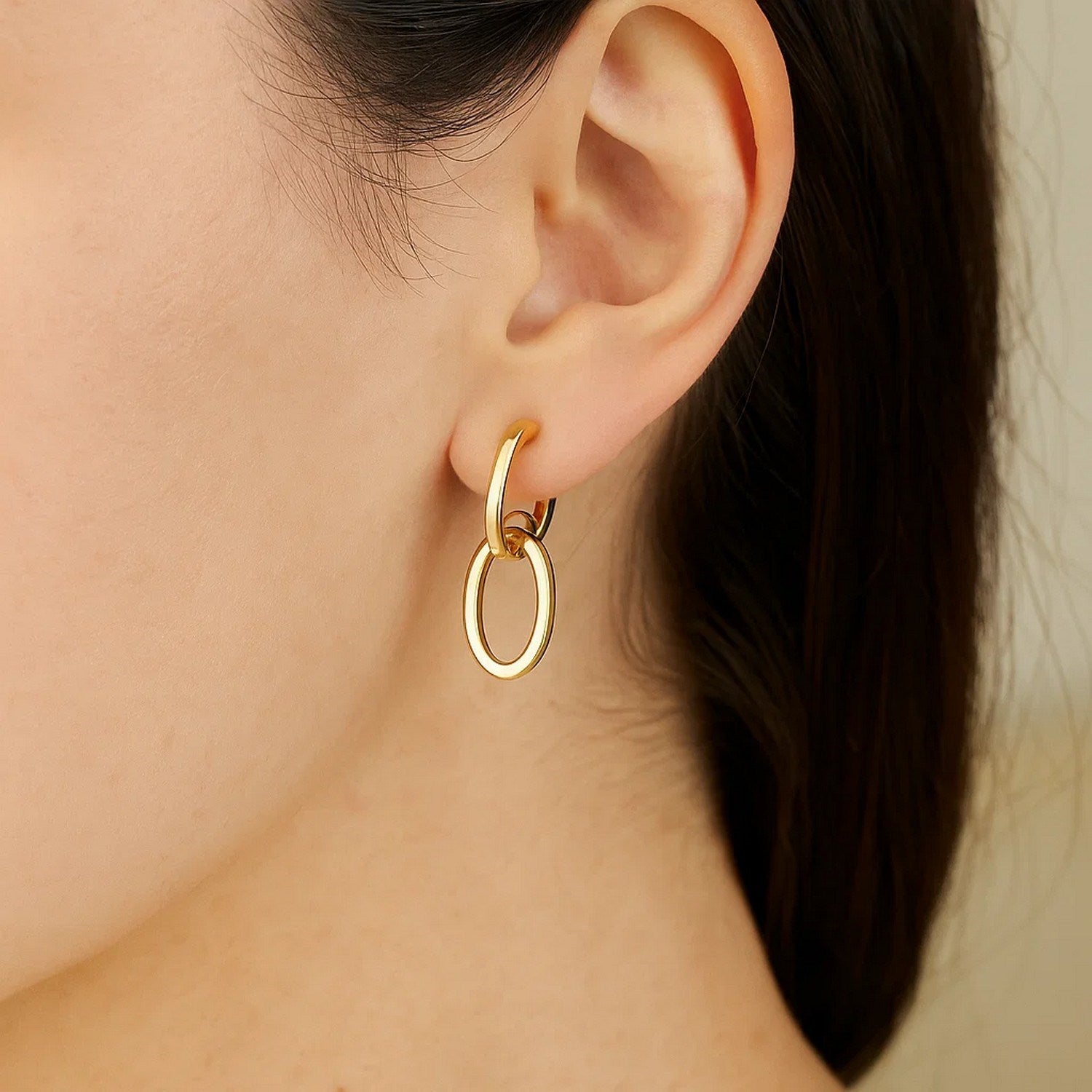 A woman wears 14K yellow gold interlocking drop hoop earrings.