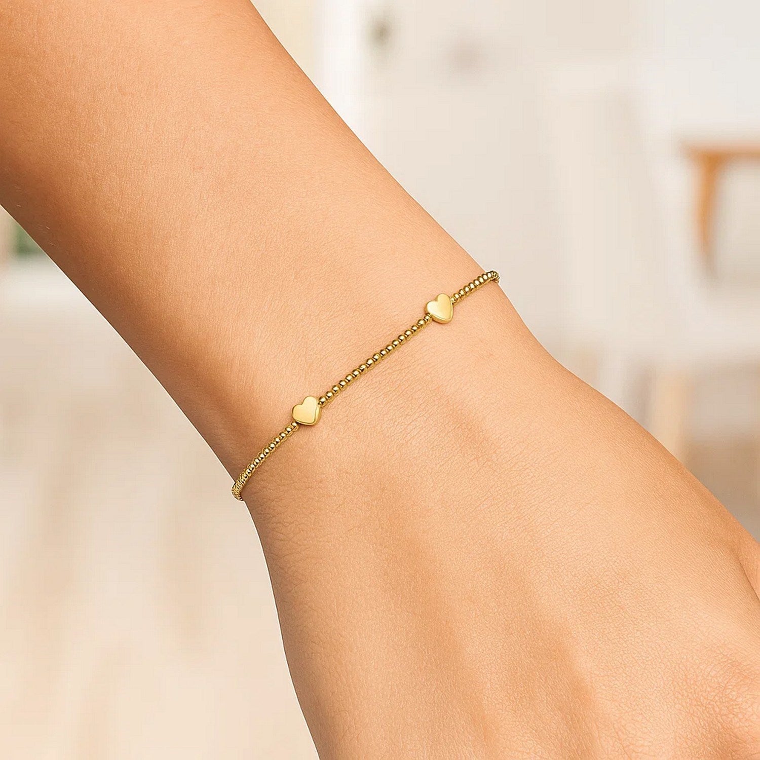 14K yellow gold bead bracelet with three heart stations on a wrist.