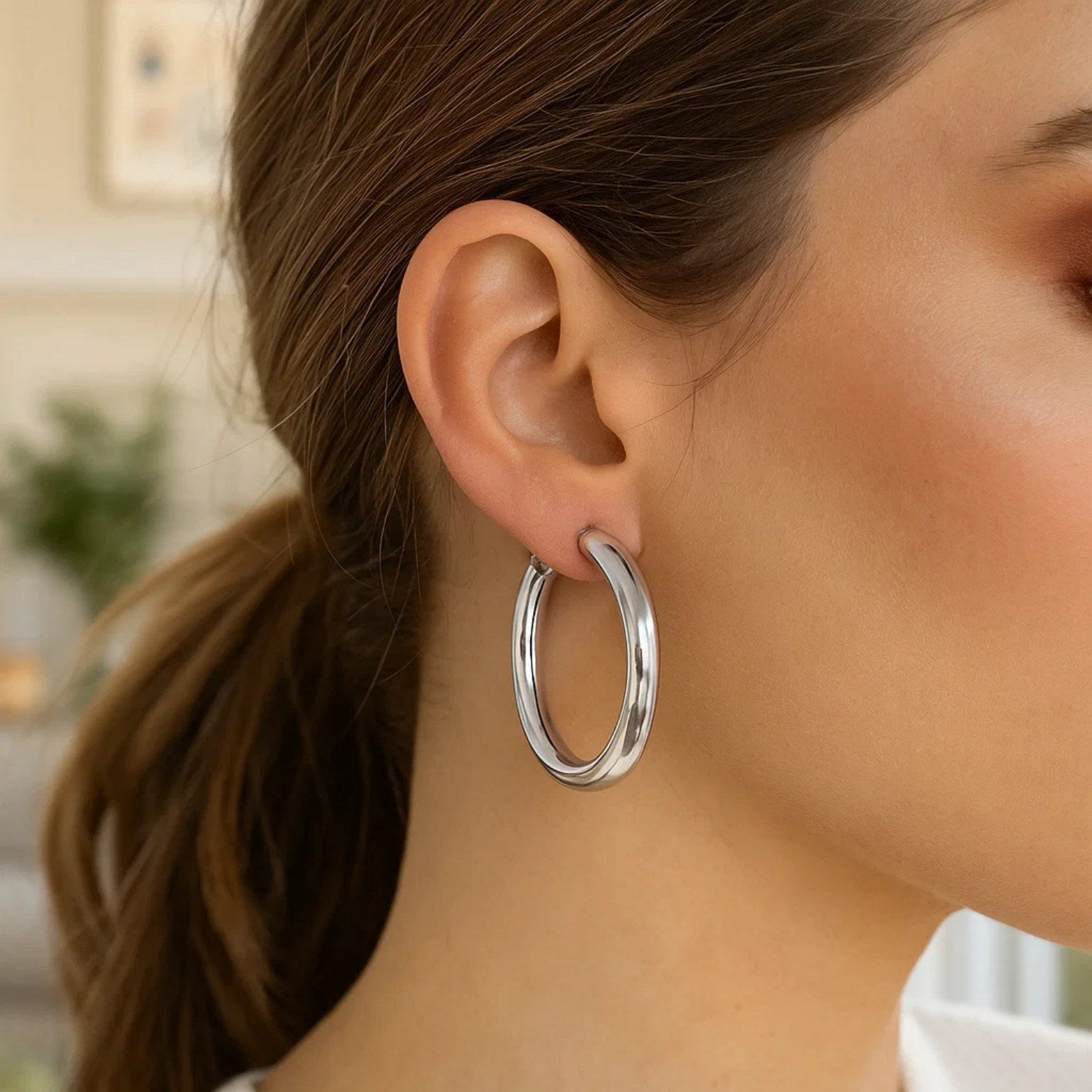 Sterling silver thick rhodium plated polished hoop style earrings on a woman's ear.