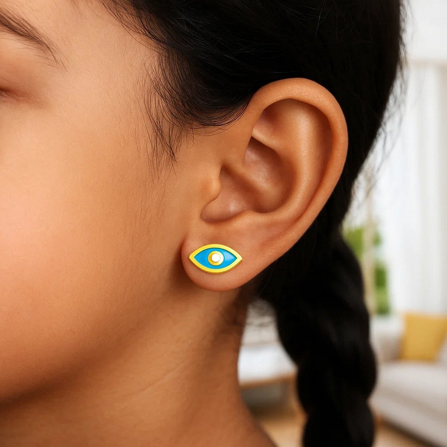 14K yellow gold blue evil eye enamel earrings on a person's ear.