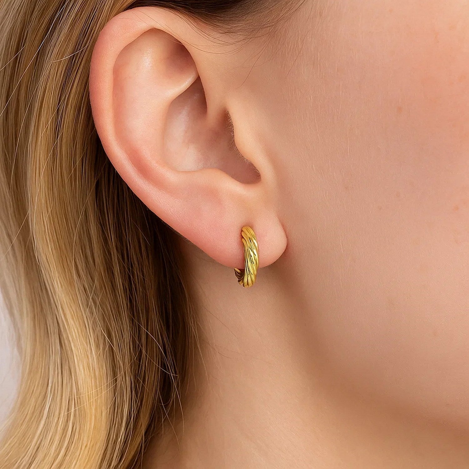 A woman wears a 14k yellow gold petite twisted round hoop earring.