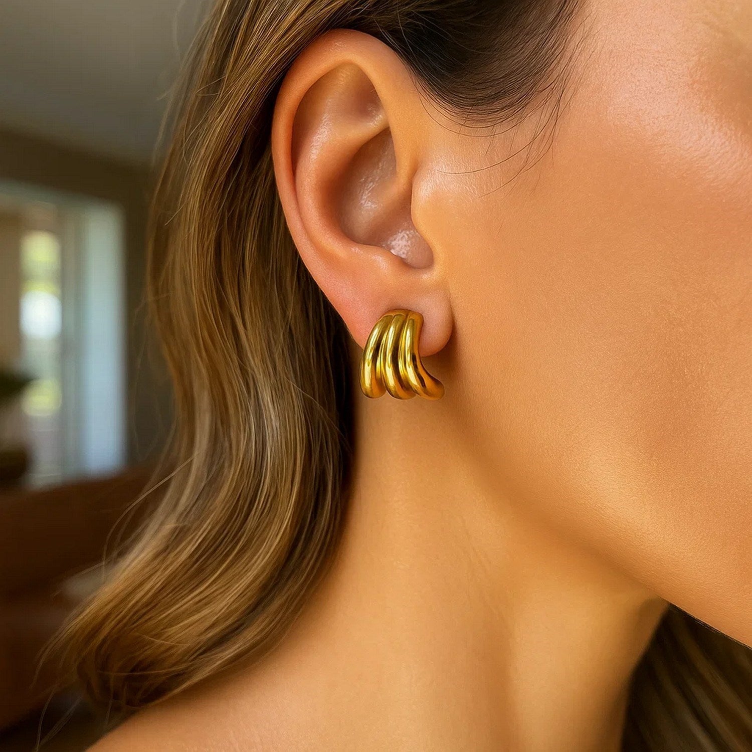 A woman wears 14K yellow gold triple row splayed hoop earrings.