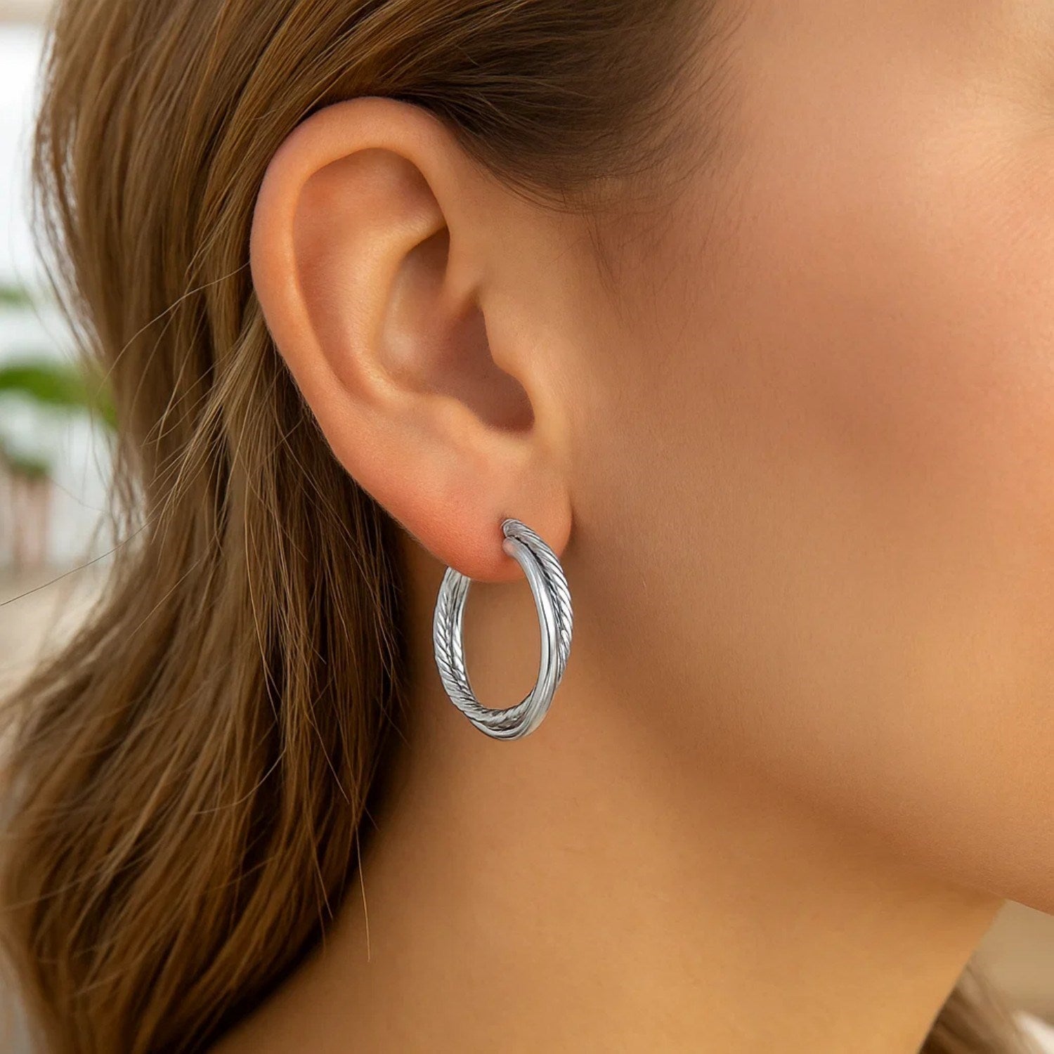 Sterling silver ridged hoop earrings with a textured design are worn on a woman's ear.