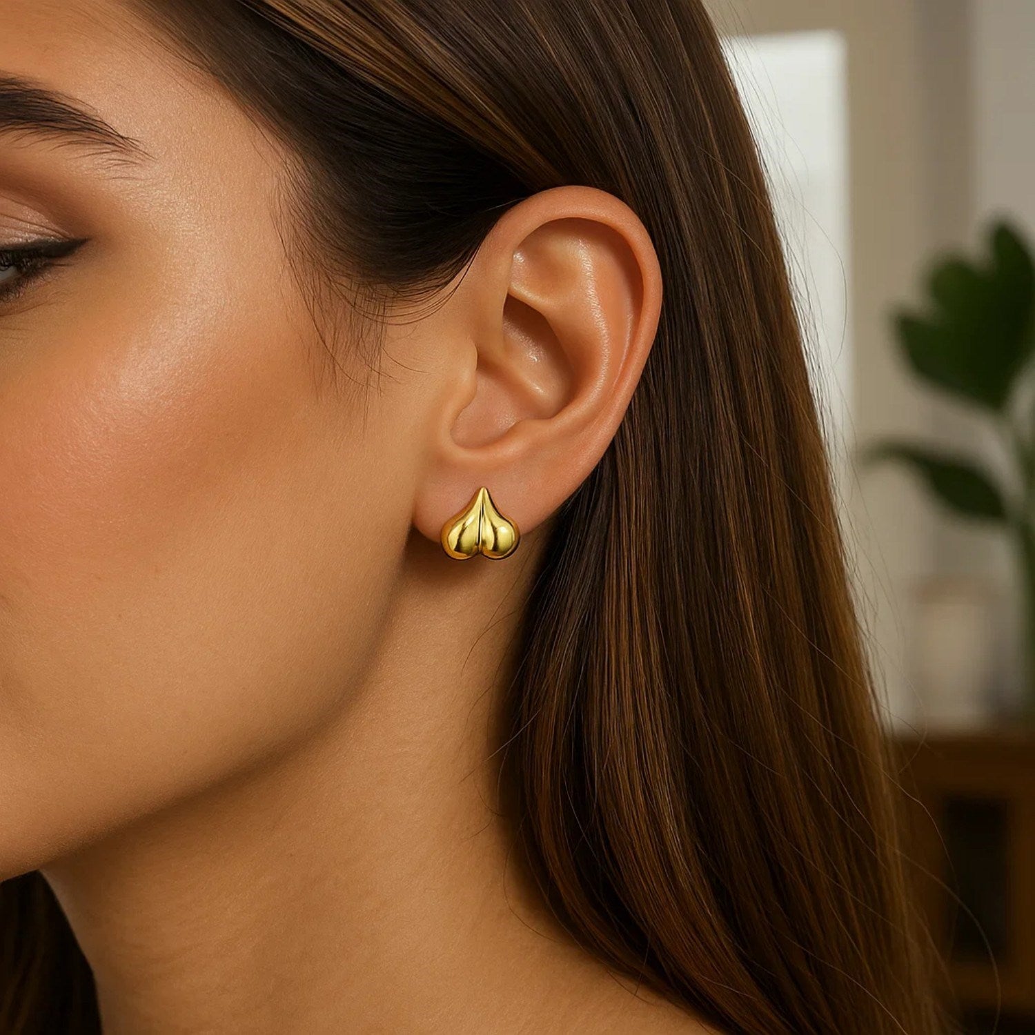 A woman wears a single 14K yellow gold puffed bubble heart stud earring.