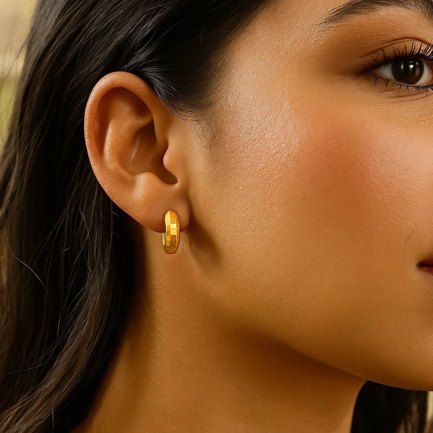 14K yellow gold checkerboard huggie hoop earring on a model's ear.