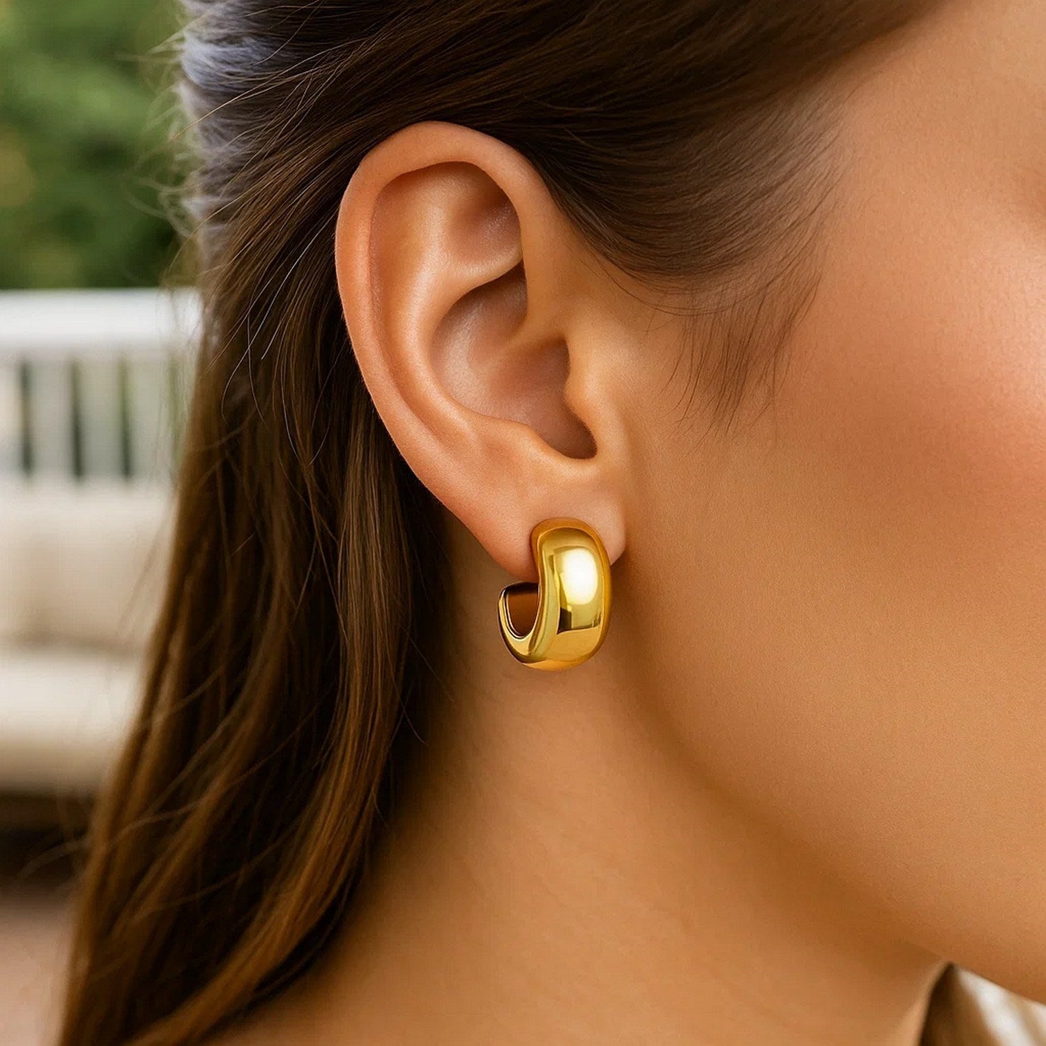 14K yellow gold polished C-hoop huggie earrings are worn on a woman's ear.
