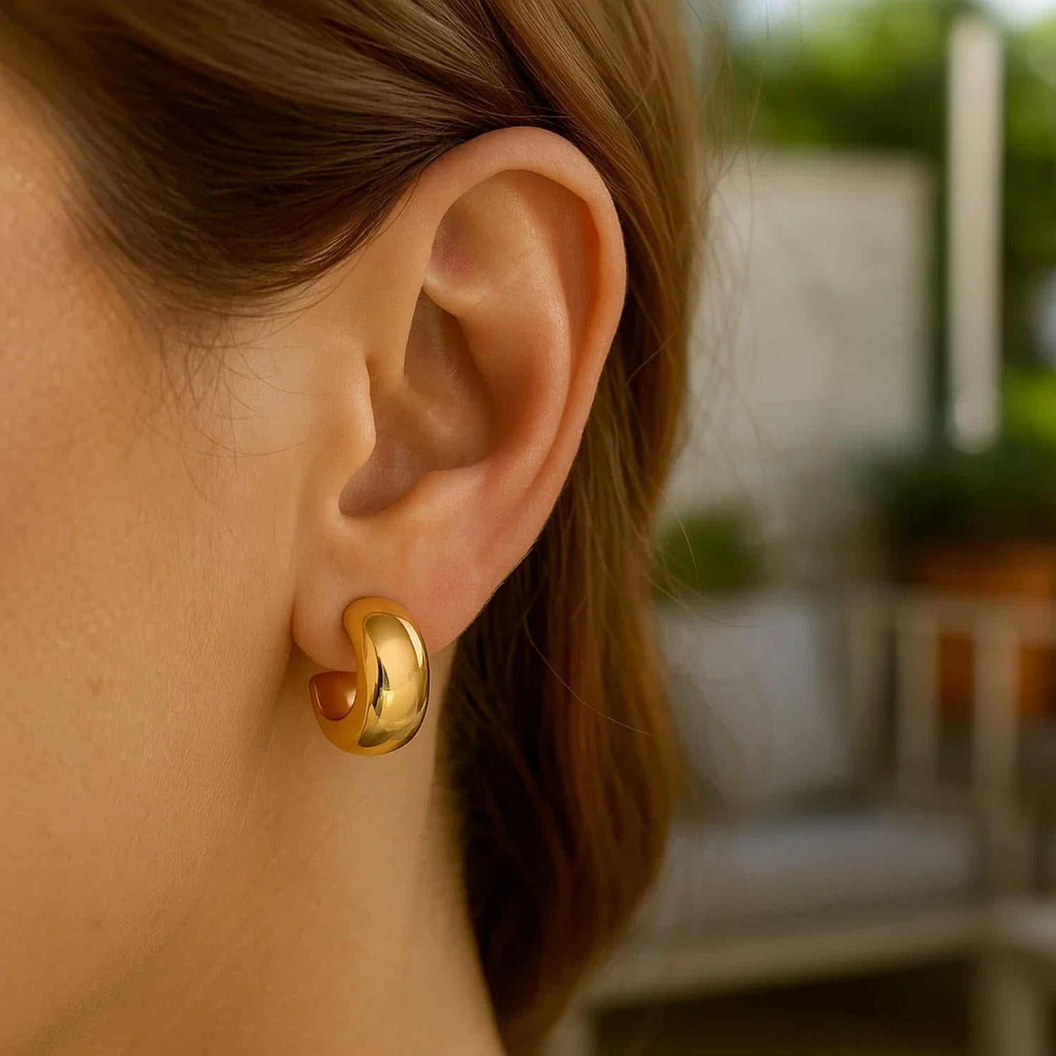 A woman wears a polished 14K yellow gold C-hoop huggie earring.