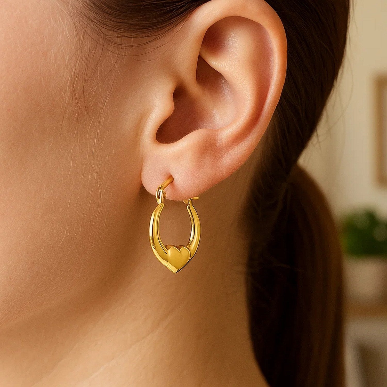 Small 14K yellow gold heart hoop earring on a person's ear.
