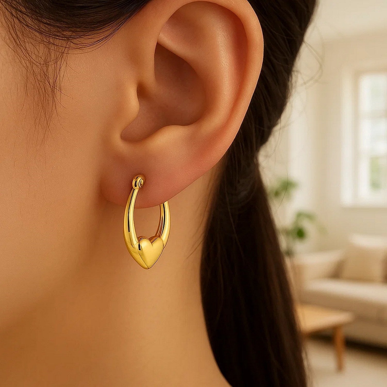 Small 14K yellow gold heart hoop earring on a person's ear.