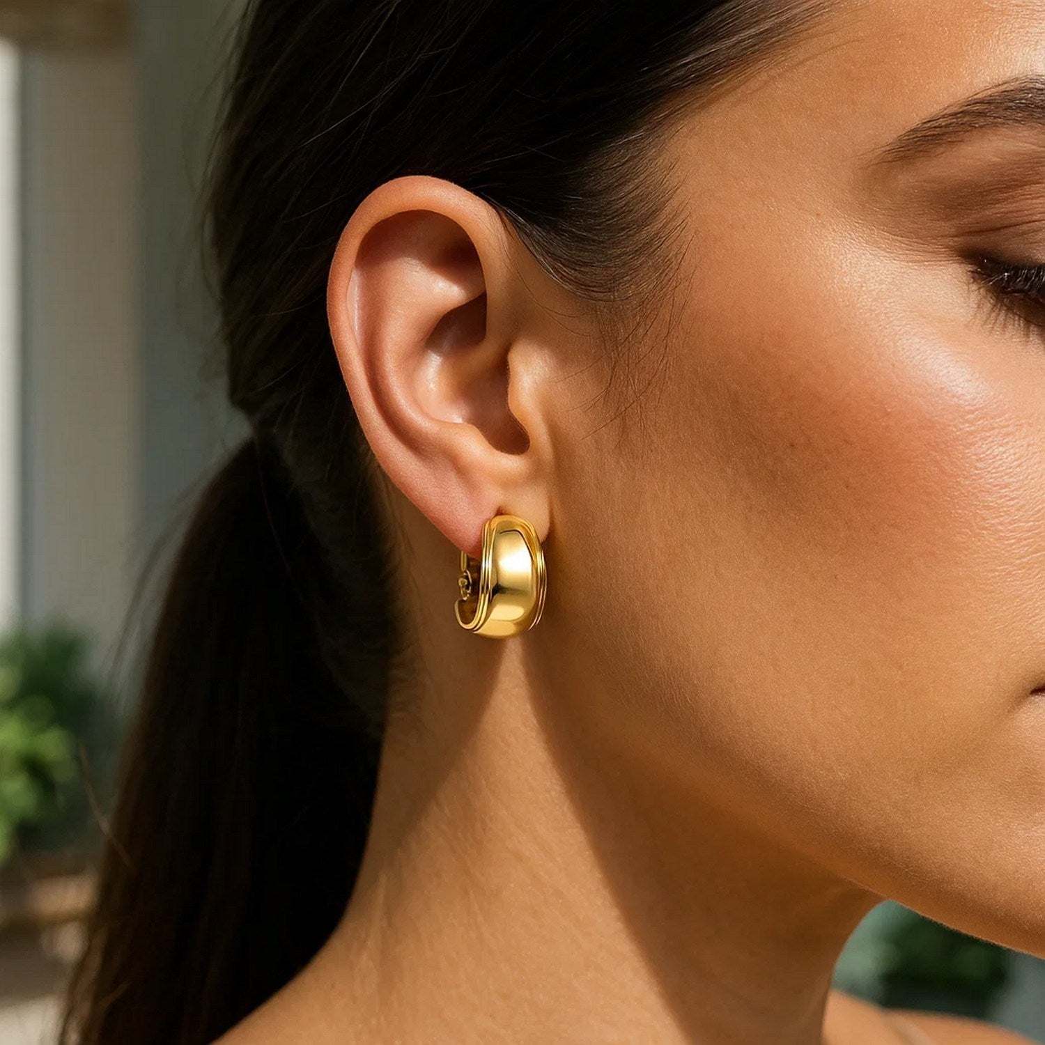 A woman wears a single 14K yellow gold omega mixed media hoop earring.