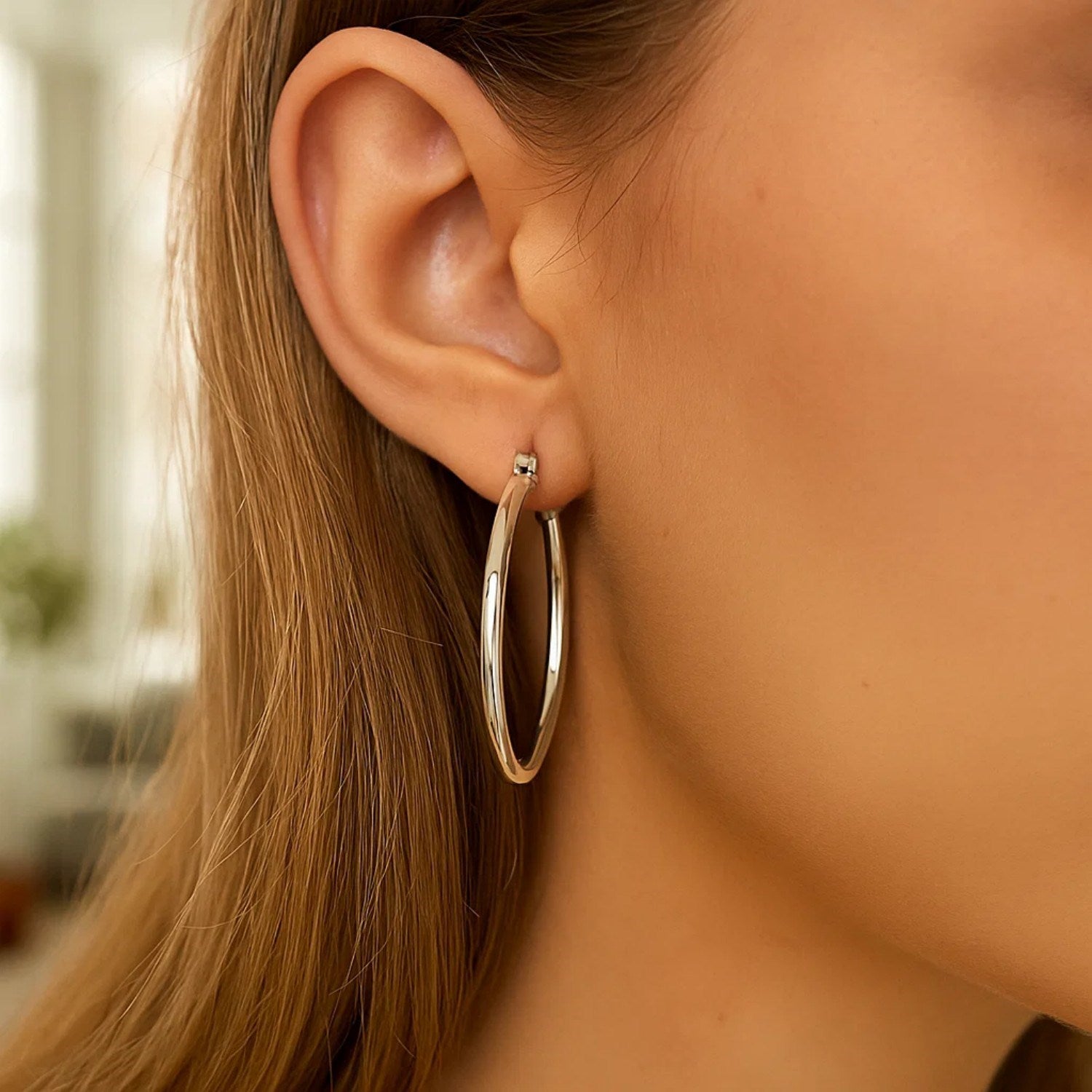 Sterling silver rhodium plated large polished classic hoop earrings on a model.