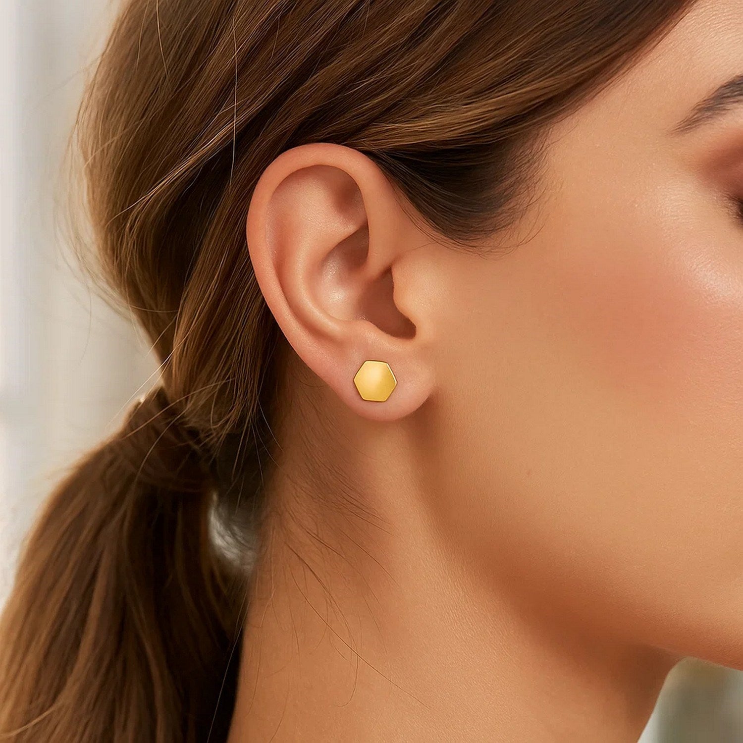 14k yellow gold hexagon stud earrings on a woman's ear.