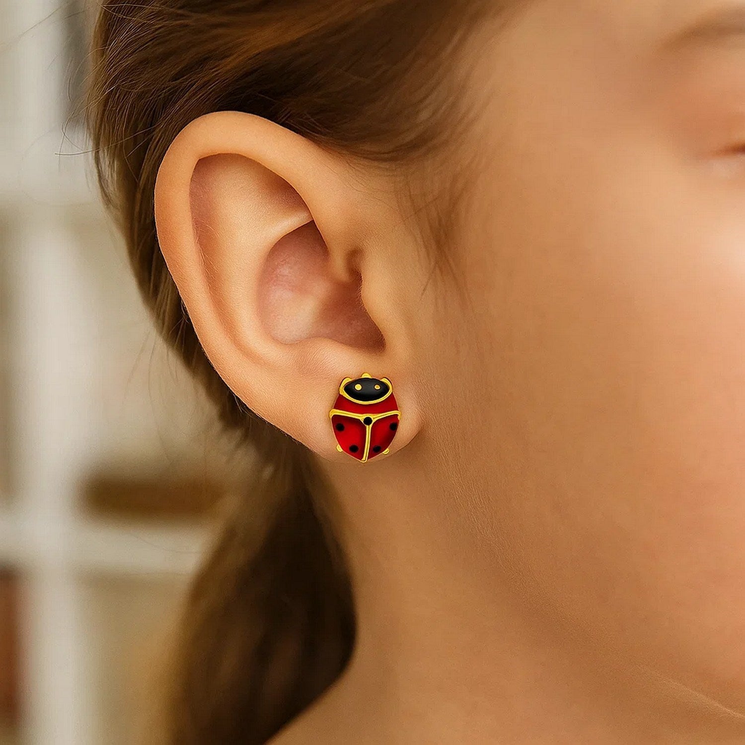A woman wears a single 14K yellow gold ladybug earring with red and black enamel.
