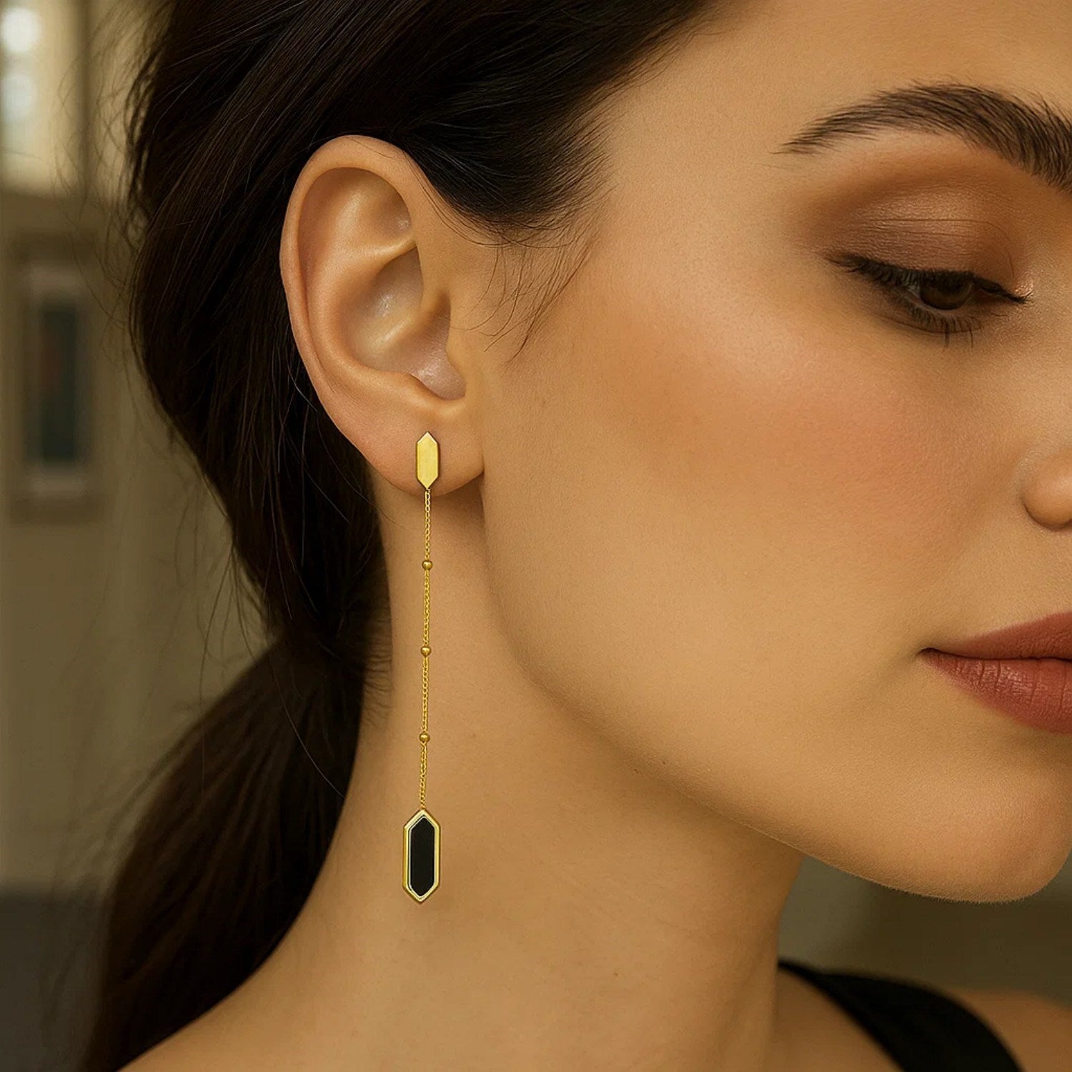 14K yellow gold hexagon onyx drop earrings on a woman's ear.