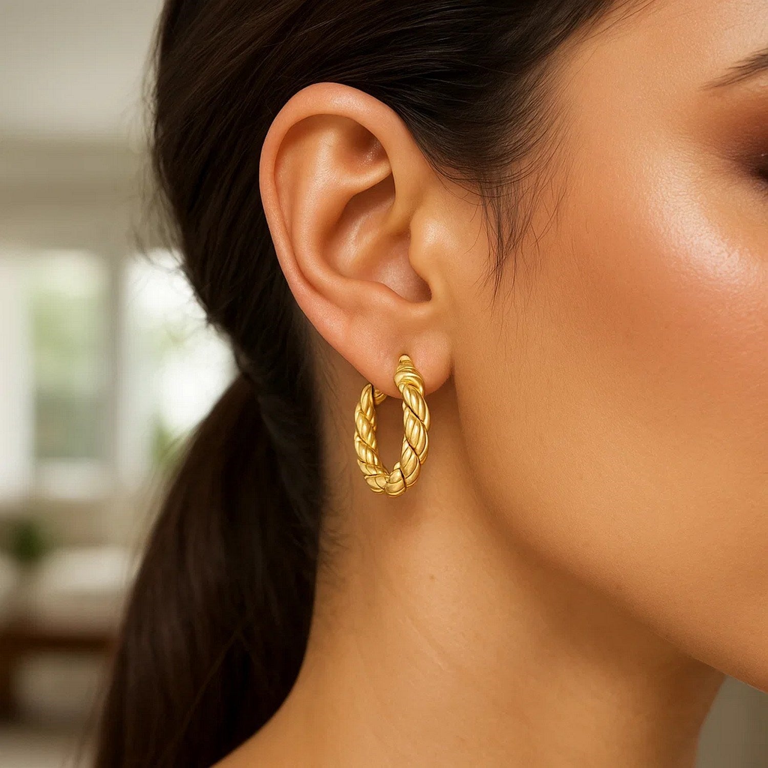 A woman wears a single 14k yellow gold rope hoop earring.