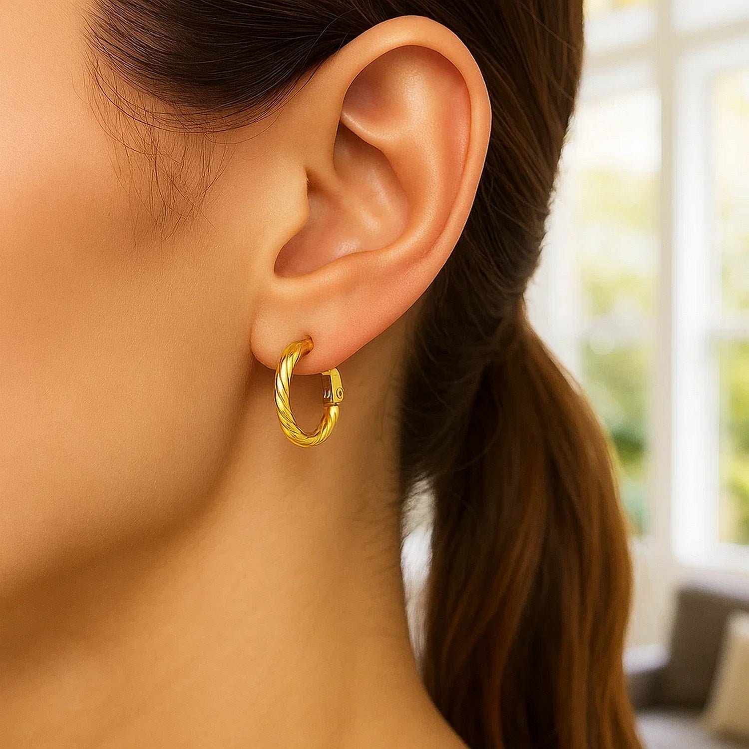 A woman wears a single 14k yellow gold twisted hoop earring.