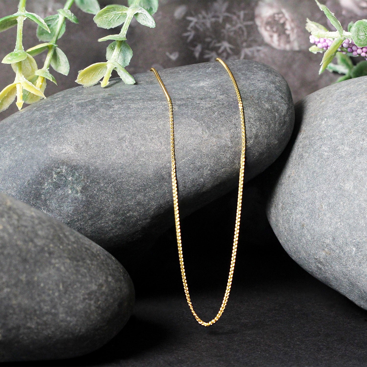 A delicate 14k yellow gold round wheat chain draped over dark grey stones.