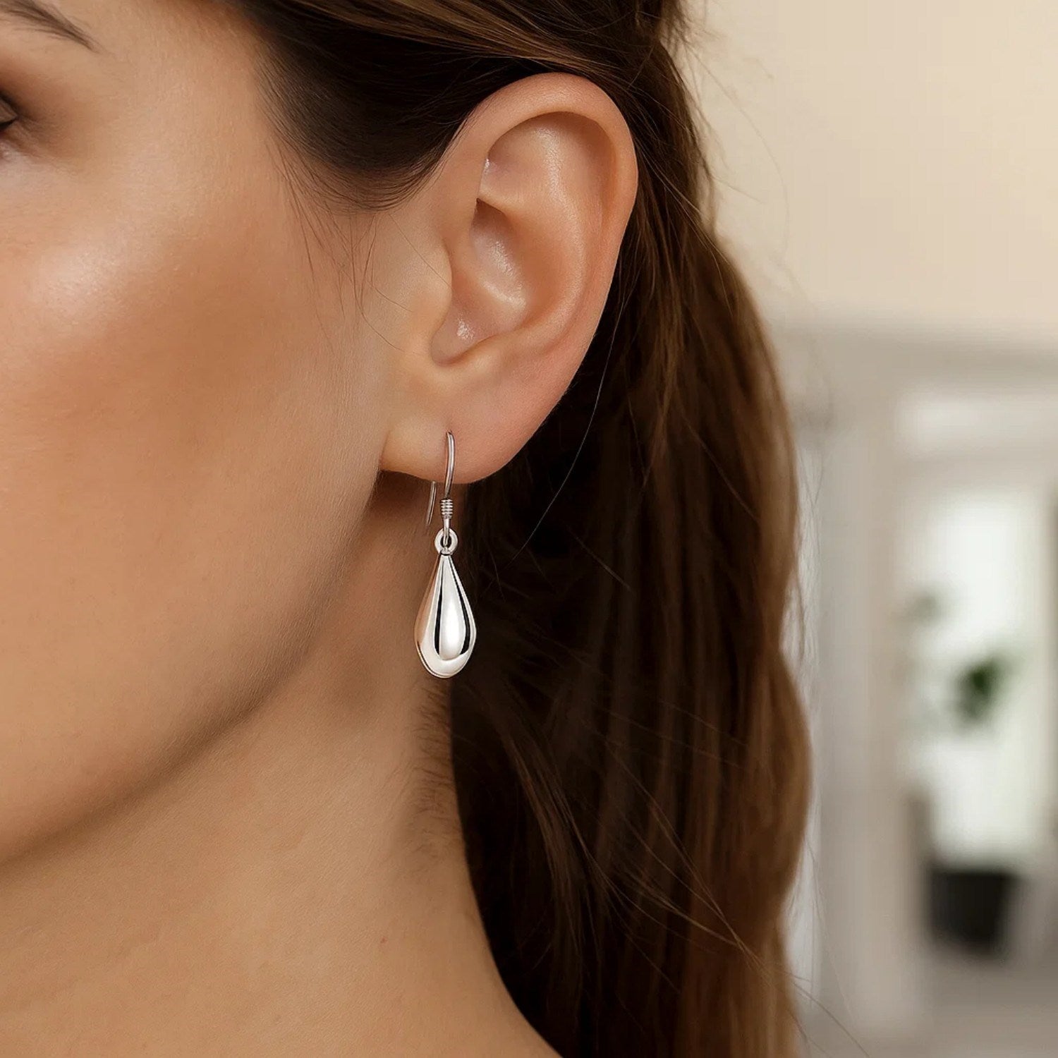 Sterling silver polished puffed teardrop dangle earrings on a woman's ear.