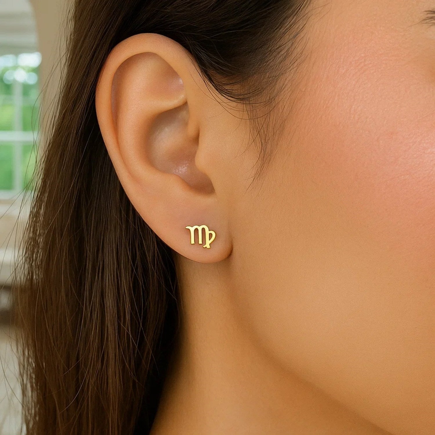 A single 14k yellow gold Virgo stud earring is worn on an ear.