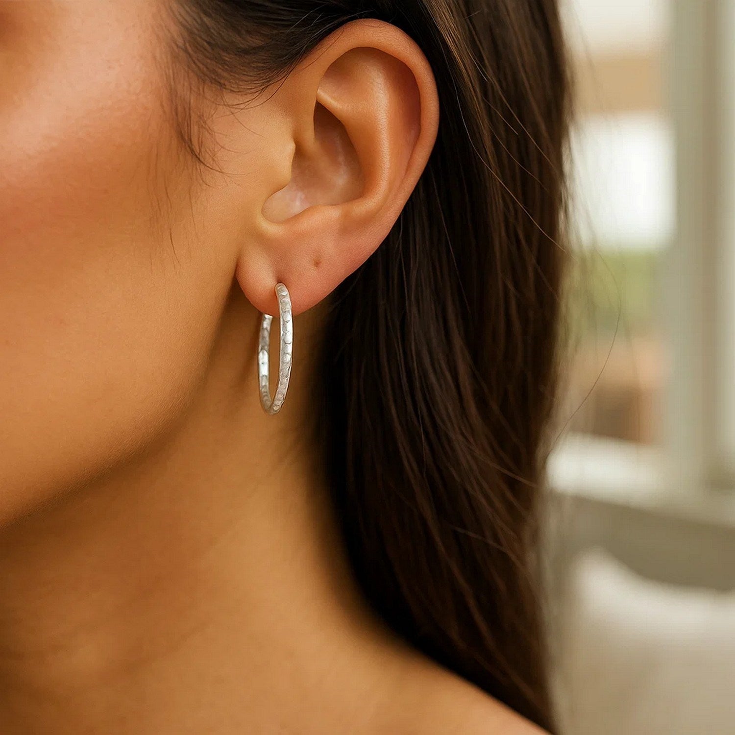 Sterling silver large hoop earrings with a hammered texture on a person's ear.