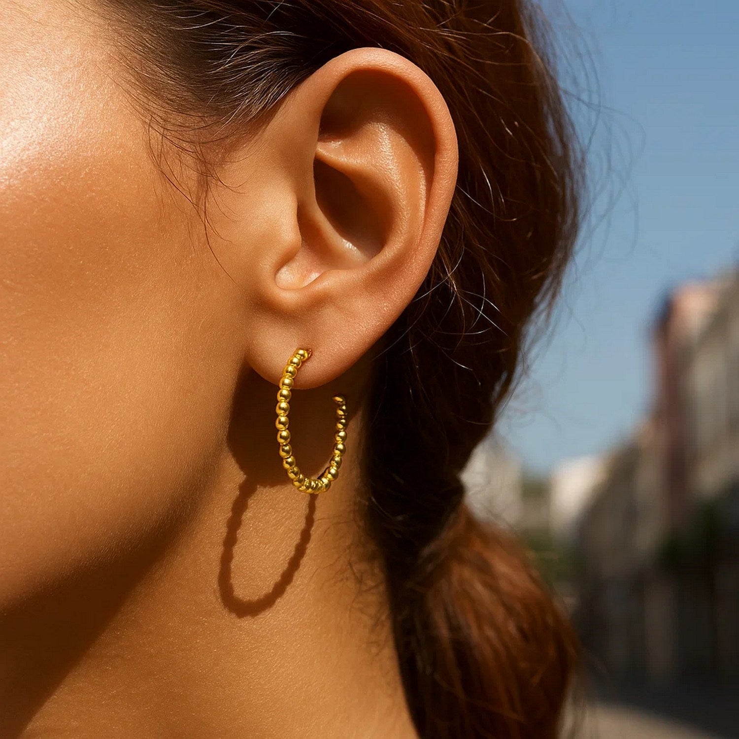 14K yellow gold bead hoop earring on a person's ear.