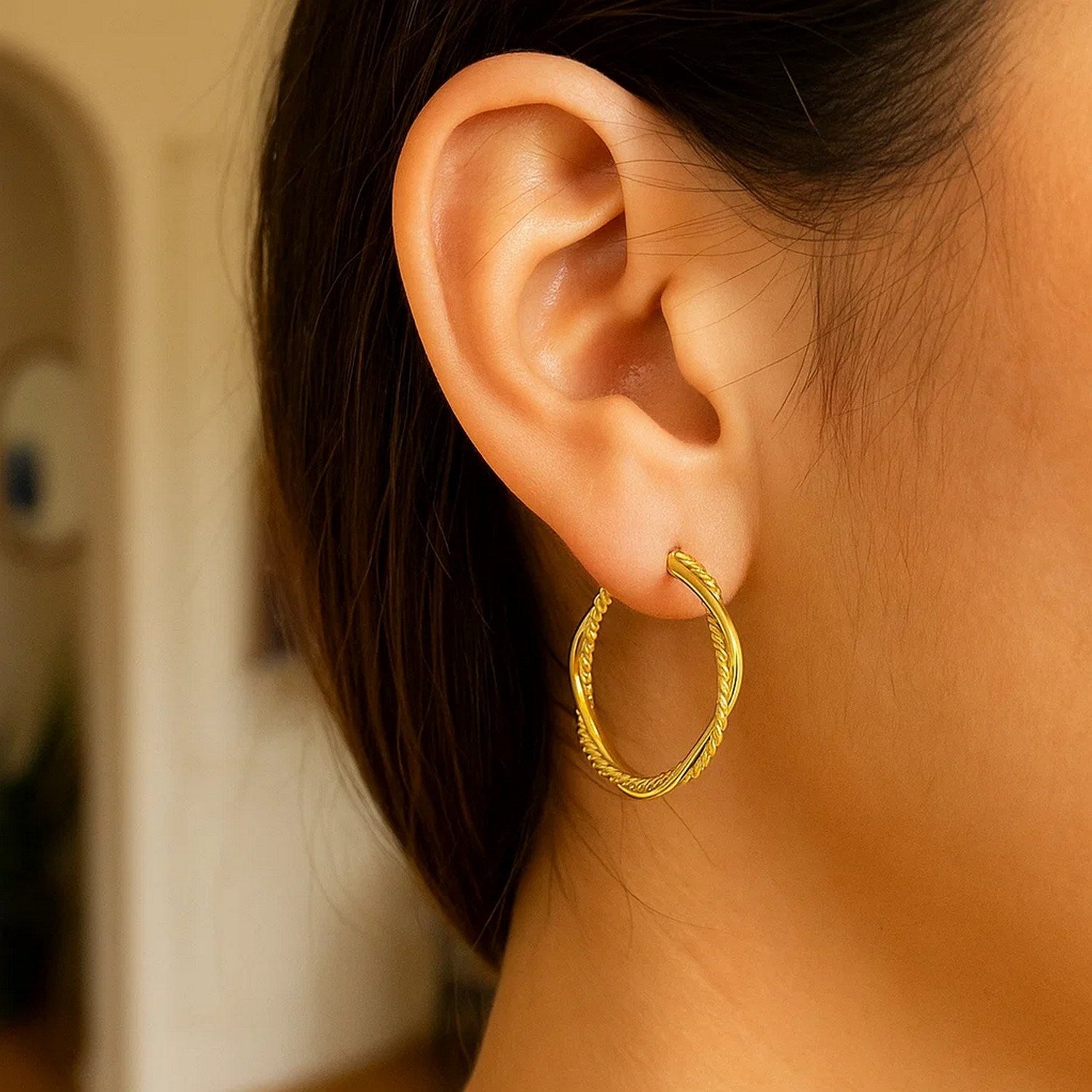 A woman wears a 14k yellow gold two-part textured twisted round hoop earring.