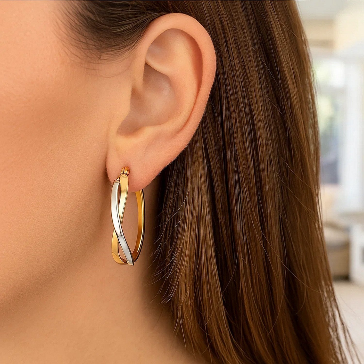 14k two-tone gold twisted style polished hoop earrings on a woman's ear.