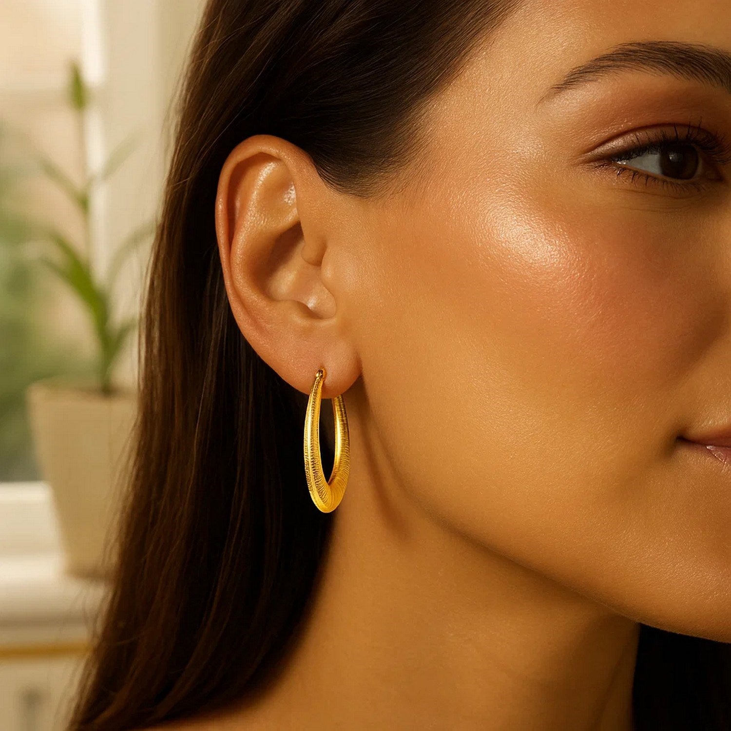 14k yellow gold graduated textured oval hoop earrings are worn on a woman's ear.