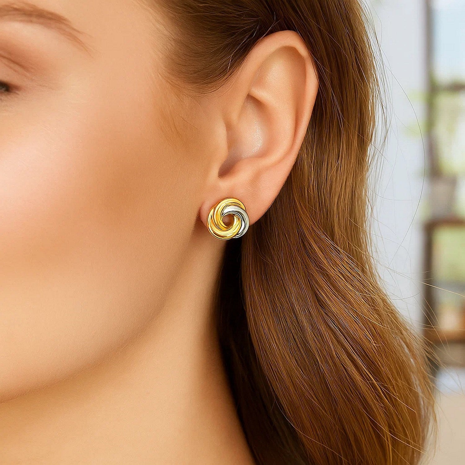Two-tone gold intertwined open circle earrings on a woman's ear.