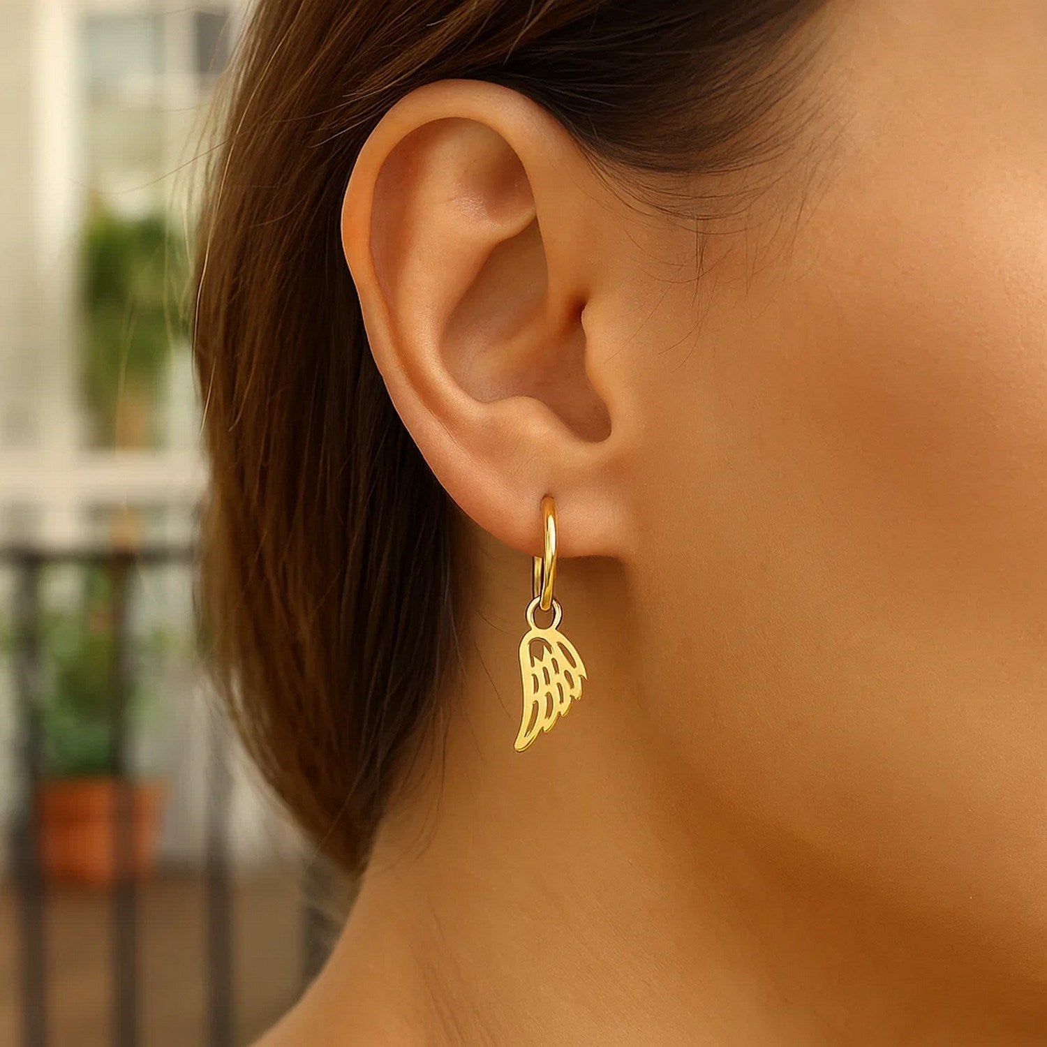14K yellow gold hoop earrings with angel wings are worn on a person's ear.