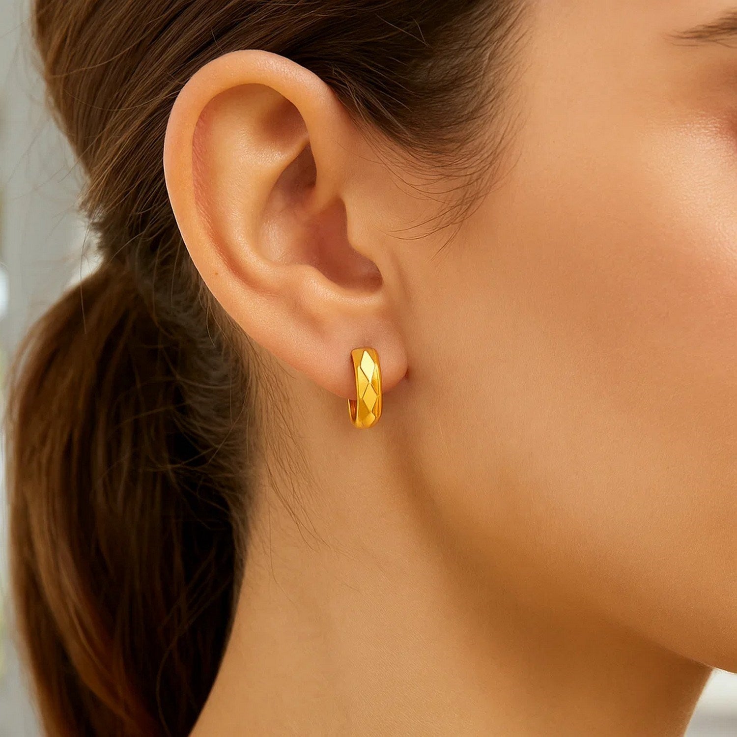 A woman wears a single 14K yellow gold faceted huggie earring with a diamond motif.