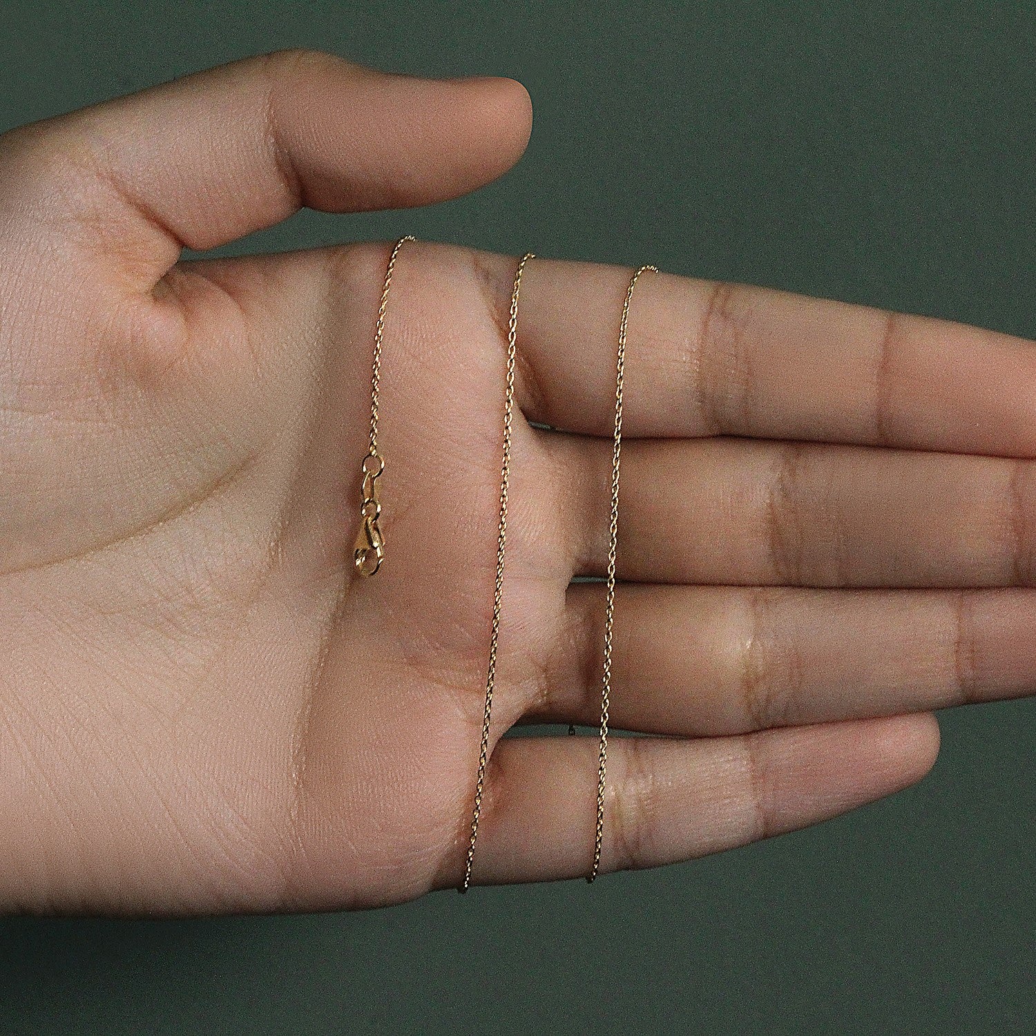 An 18k yellow gold round cable link chain with a lobster clasp rests on a hand.