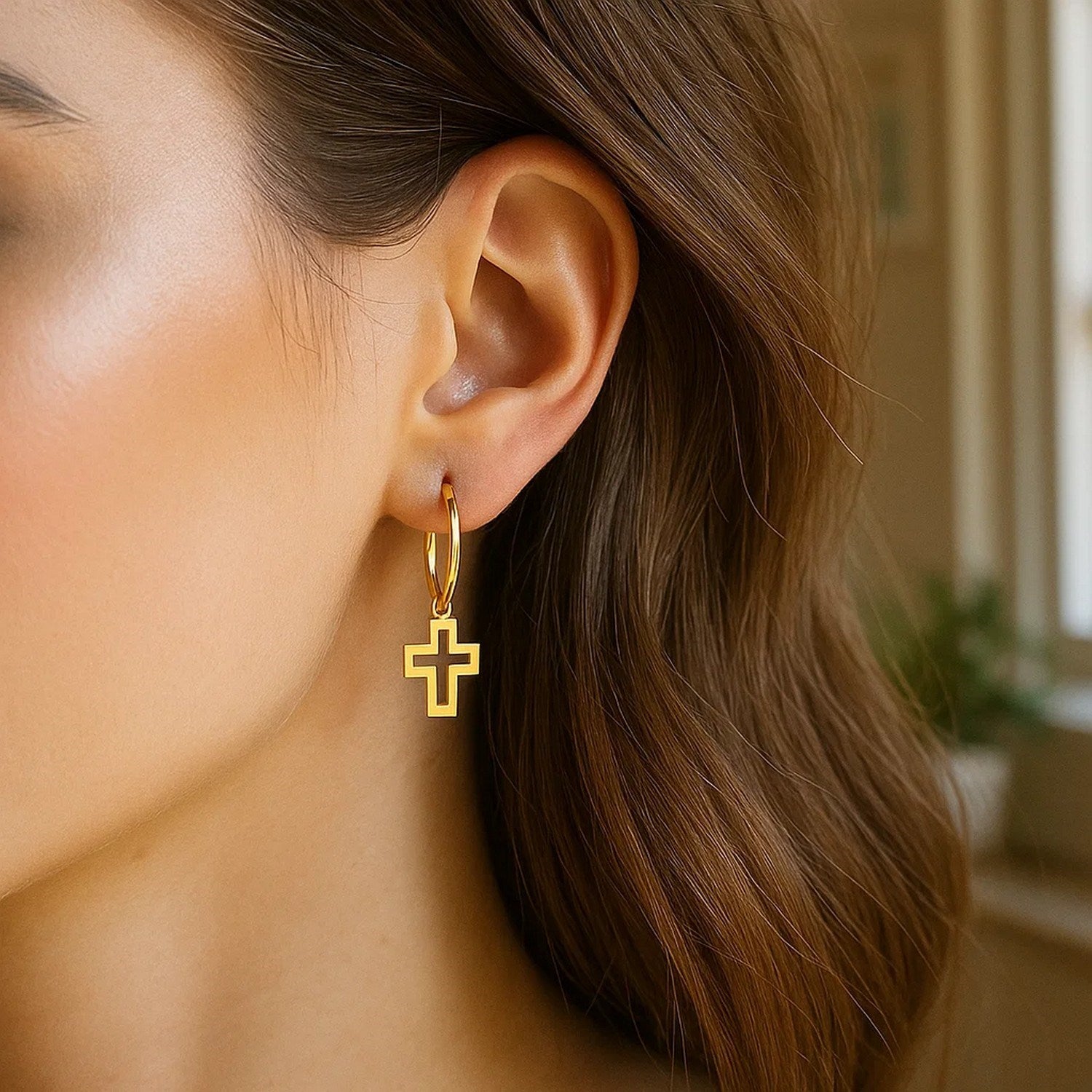 14K yellow gold hoop earrings with cross charms are worn on a woman's ear.