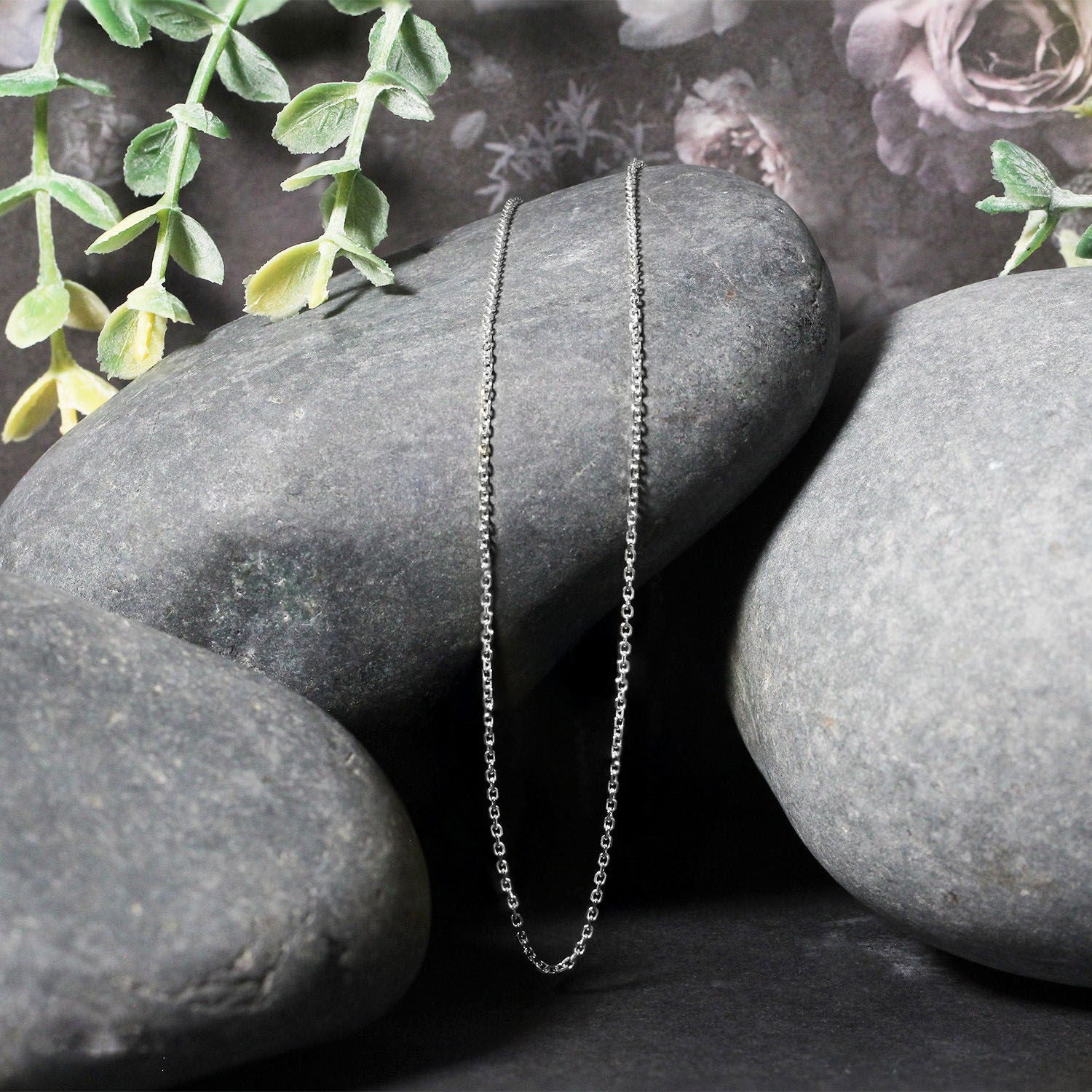 An 18k white gold diamond cut cable link chain draped over smooth gray stones.