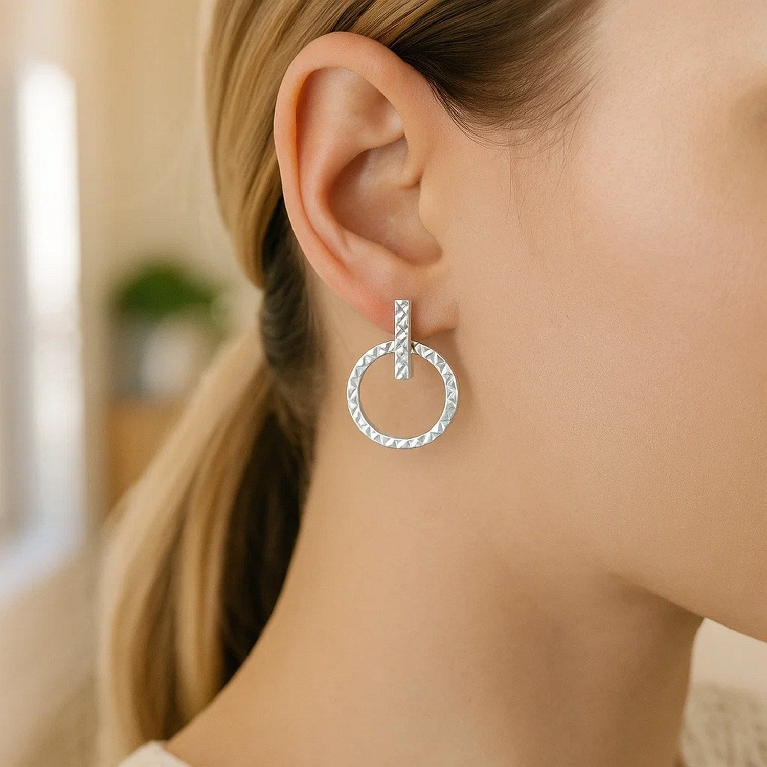 14k white gold textured circle and bar post earrings on a woman's ear.