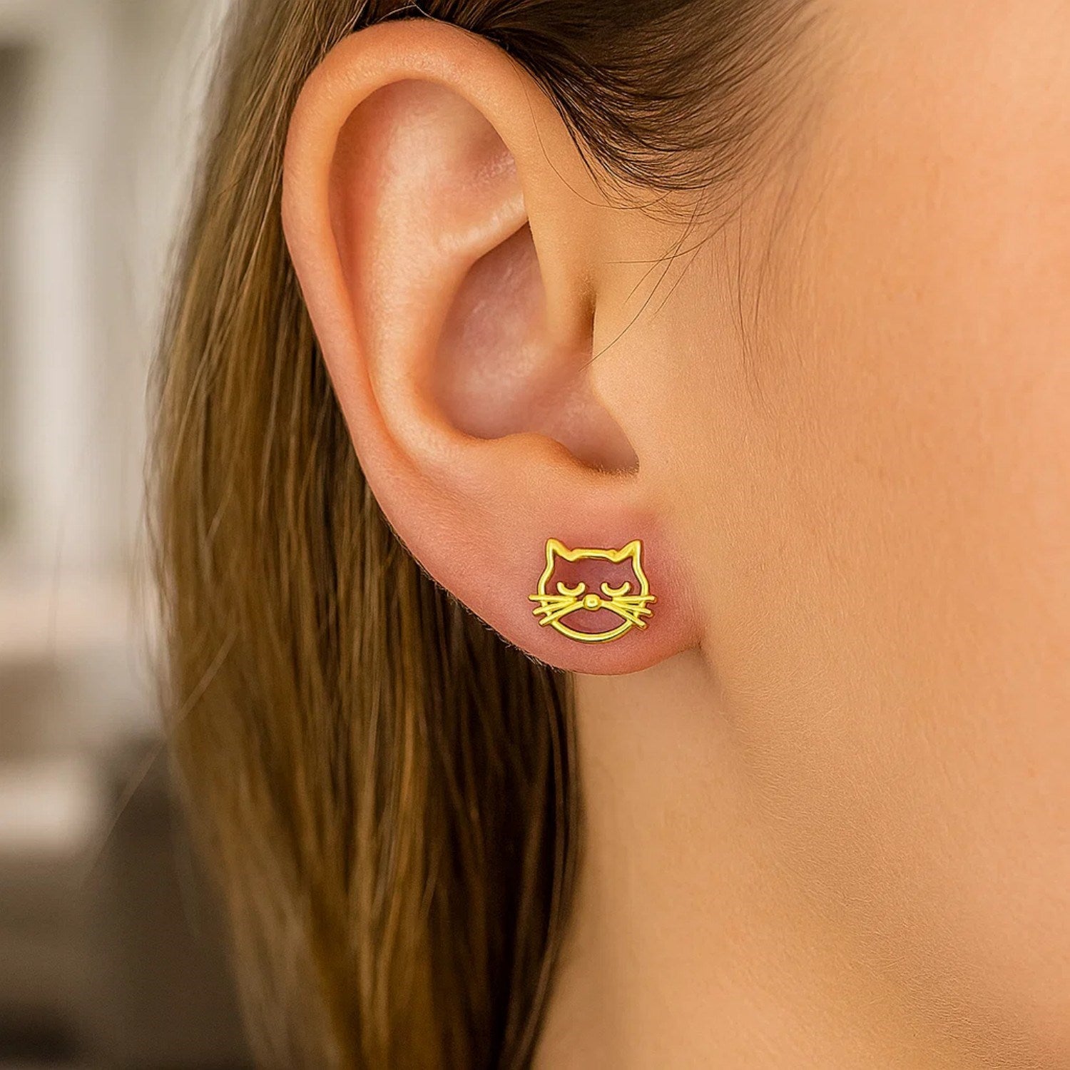 A woman wears a single 14K yellow gold cat head earring on her earlobe.