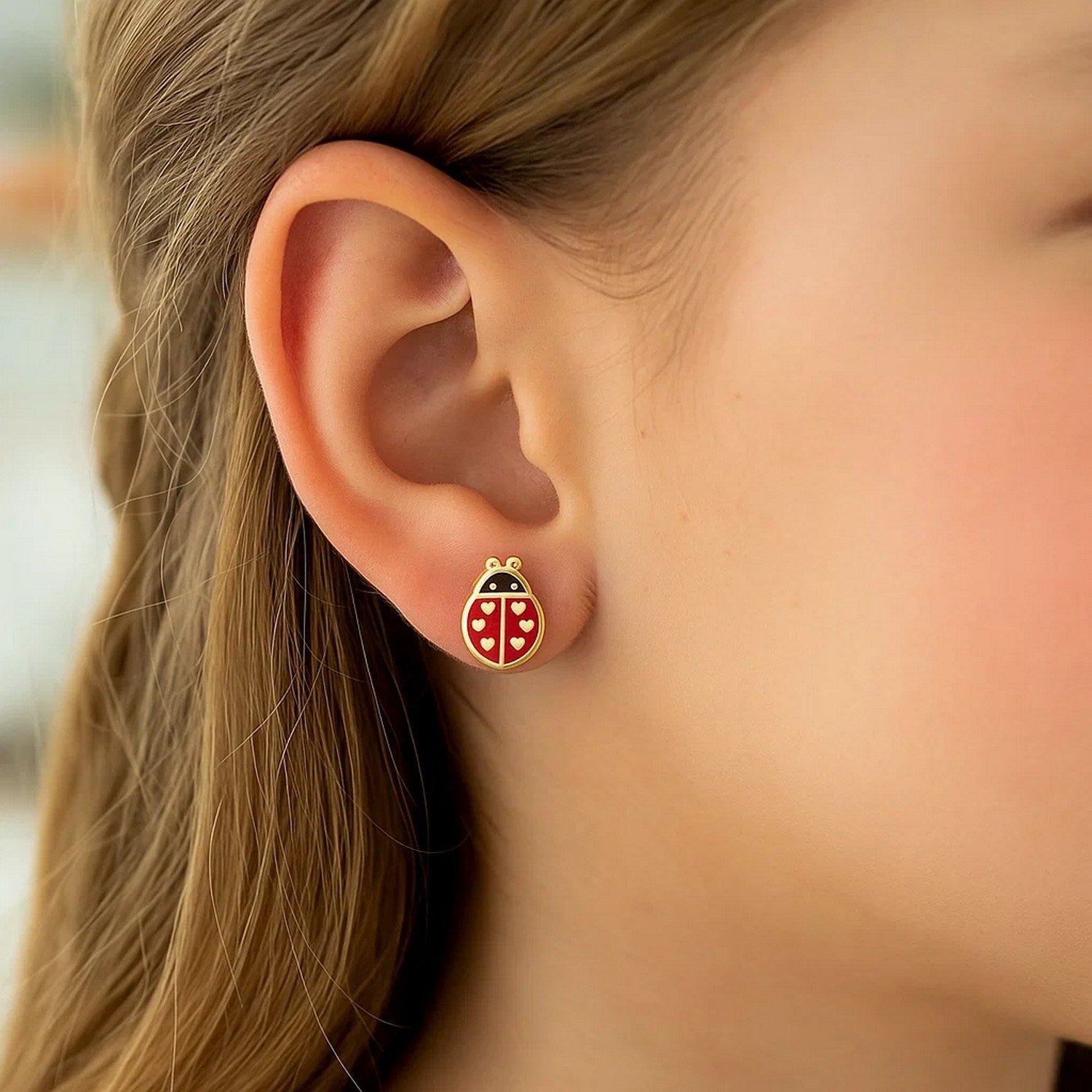 A close-up of a person wearing a 14K yellow gold ladybug enamel earring.