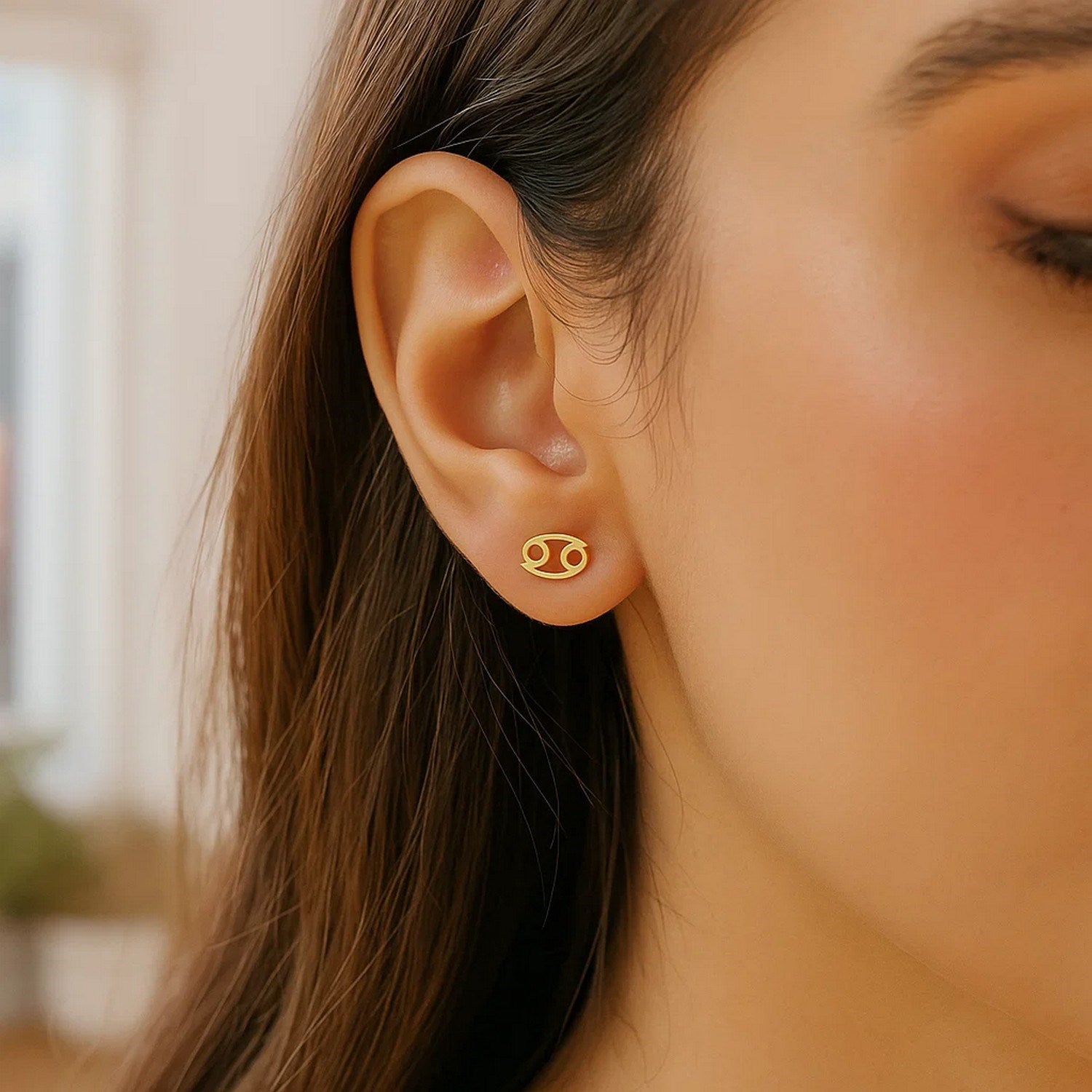 A woman wears a 14k yellow gold Cancer stud earring.