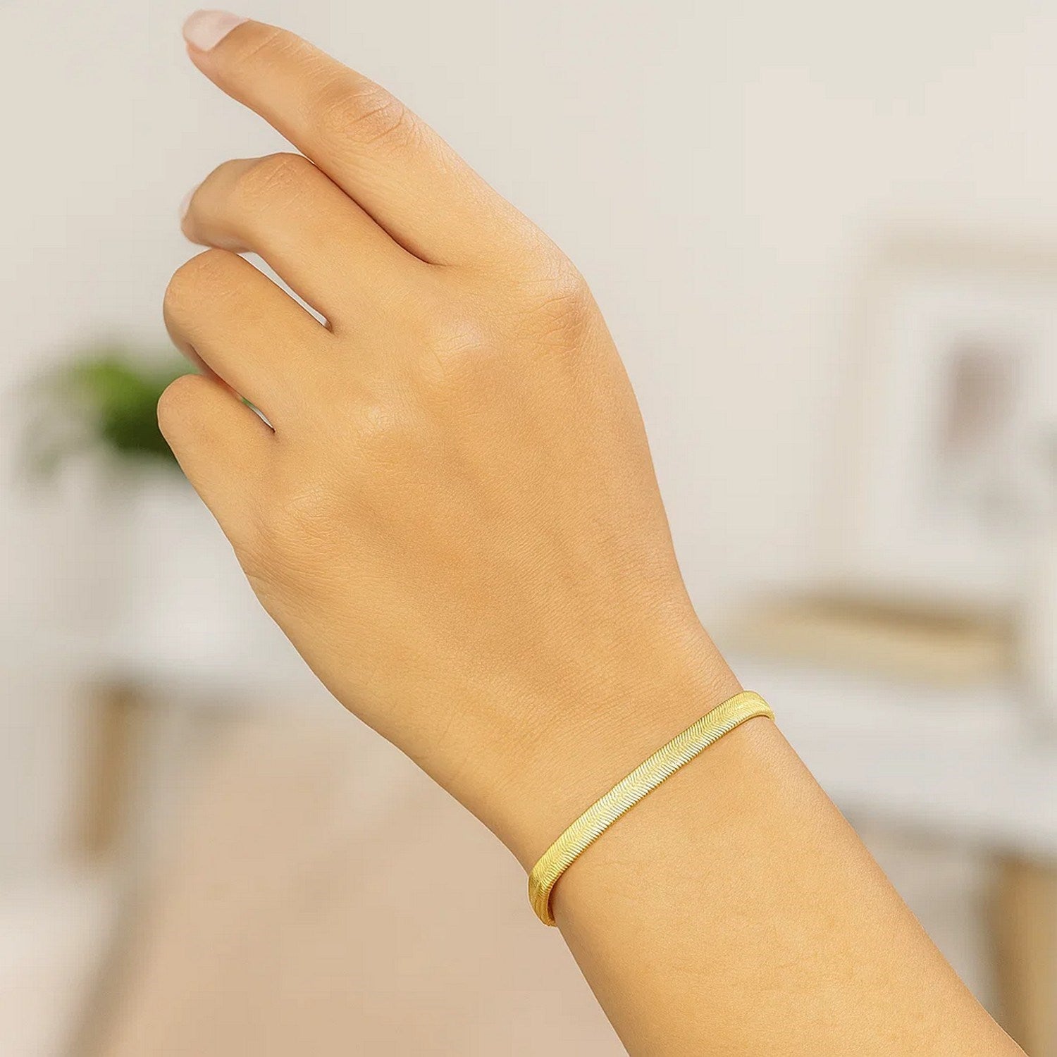 A gold herringbone bracelet is worn on a person's wrist.