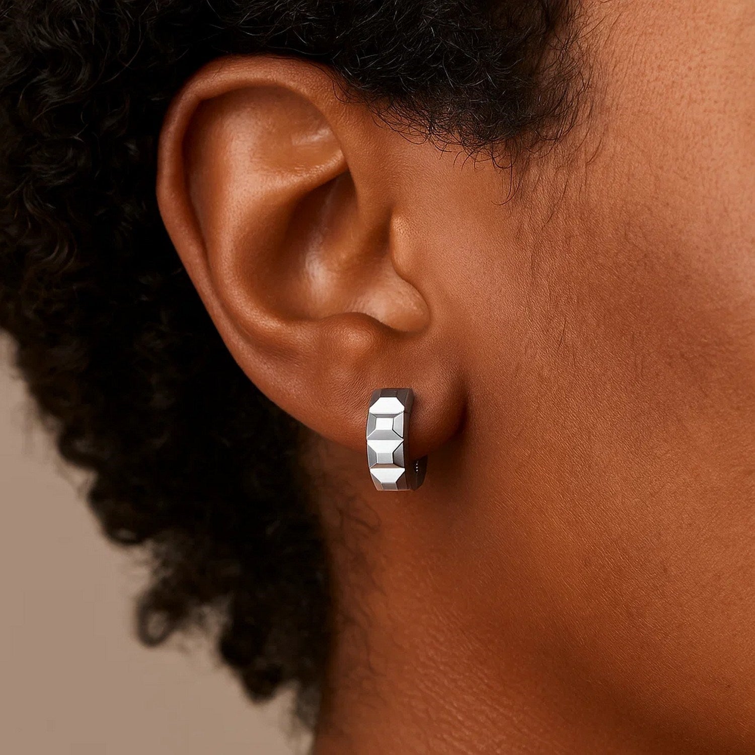 A 14K white gold square motif faceted huggie earring on an ear.