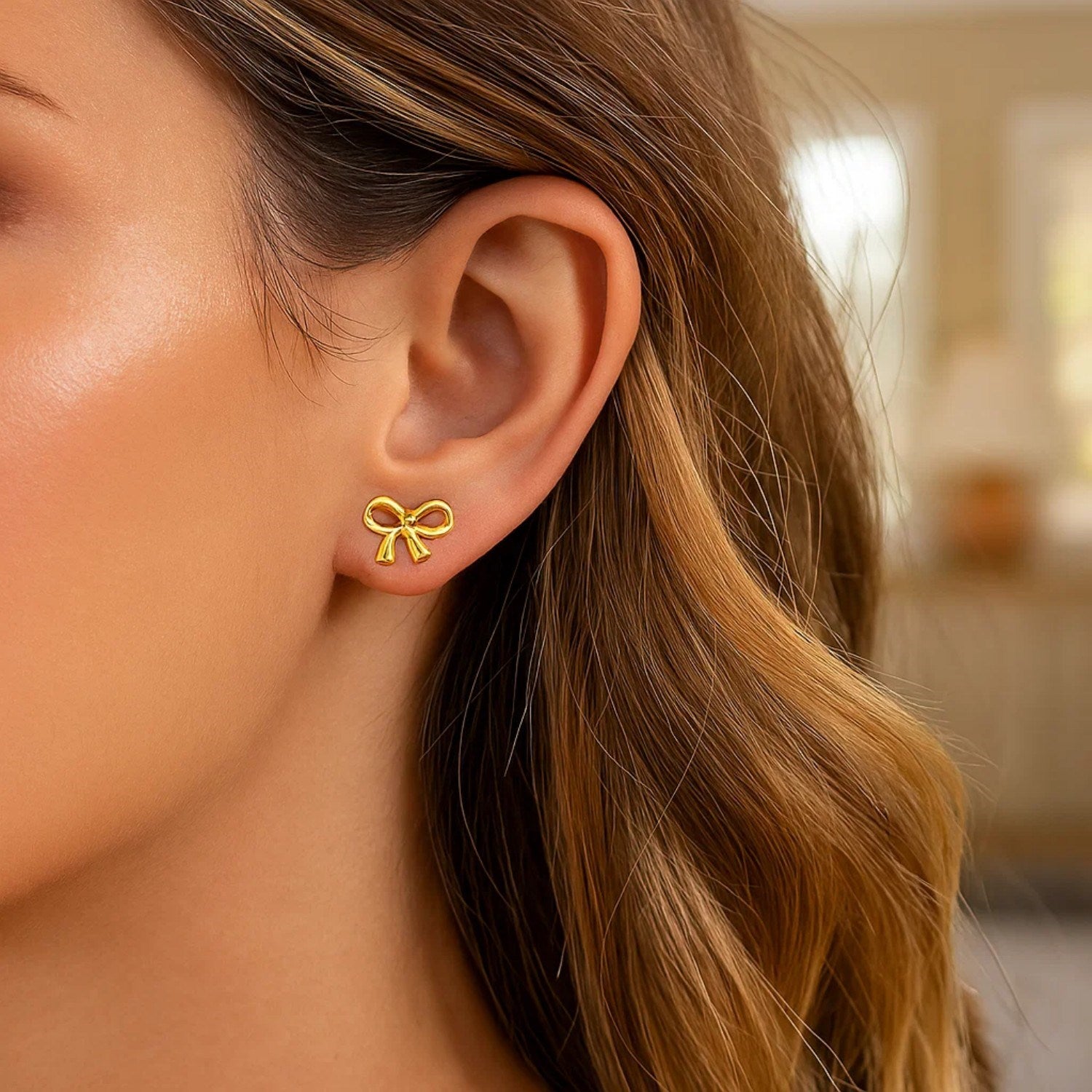 14k yellow gold bow-style post earrings on a woman's ear.