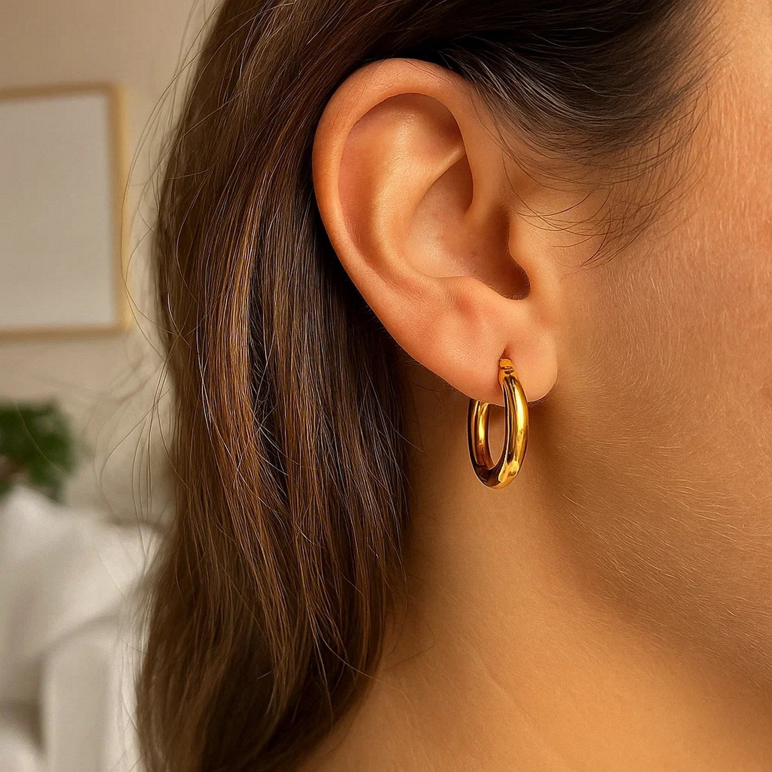 A woman wears a single 10k yellow gold polished hoop earring.