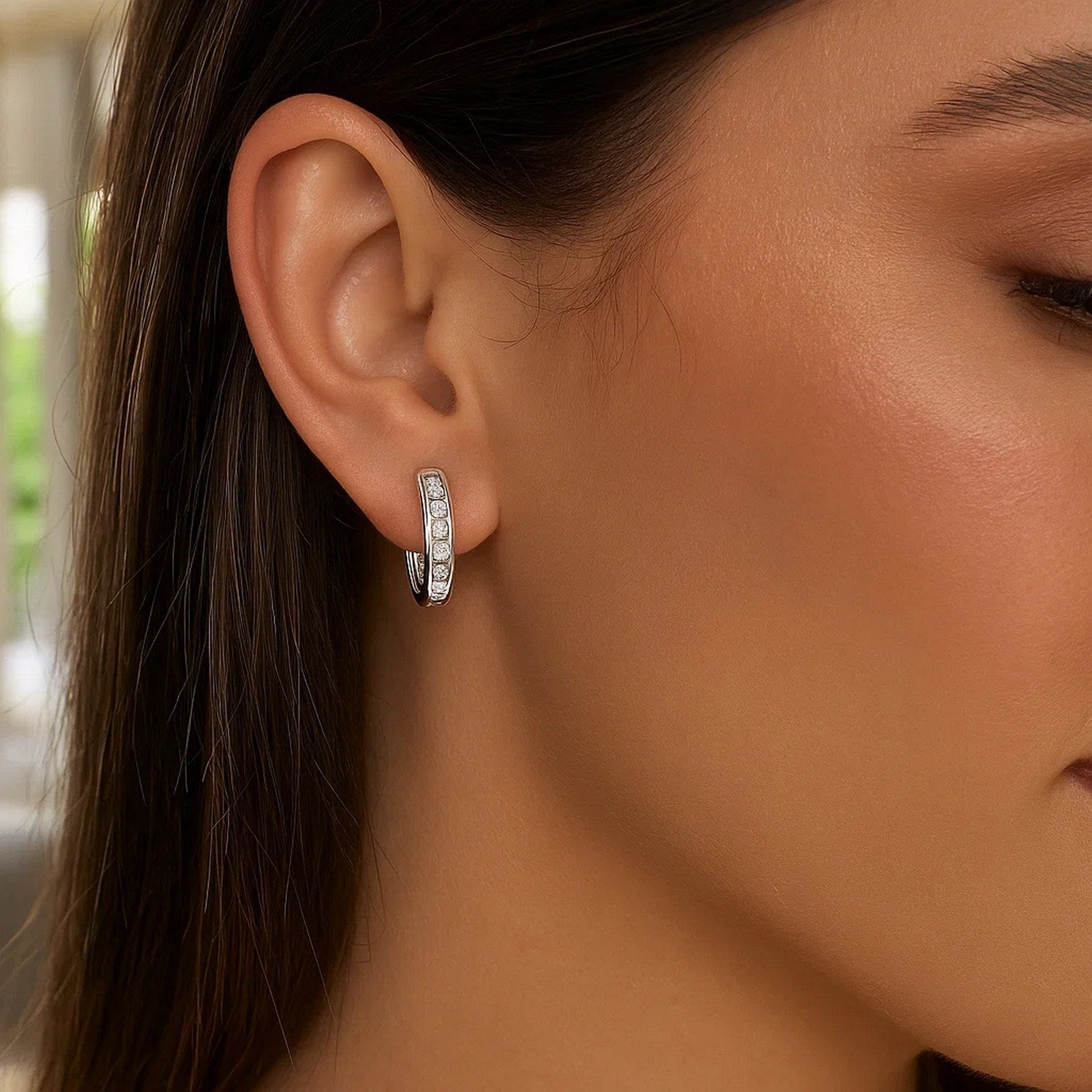 Sterling silver oval hoop earrings with cubic zirconias on a woman's ear.