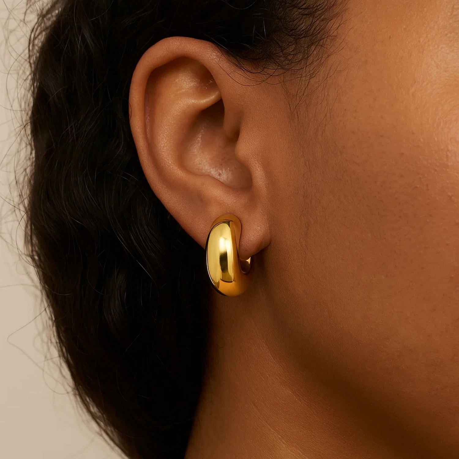14k yellow gold small omega C hoops on an ear.
