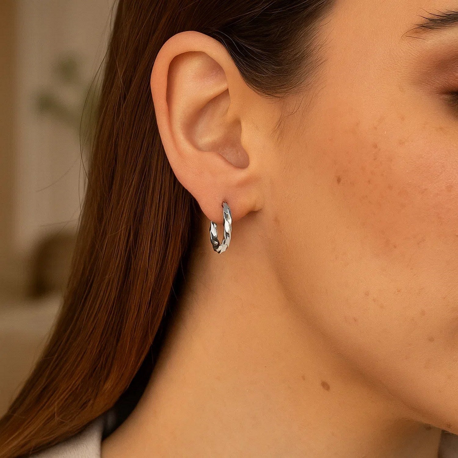 Spiral style polished hoop earrings in sterling silver on a woman's ear.