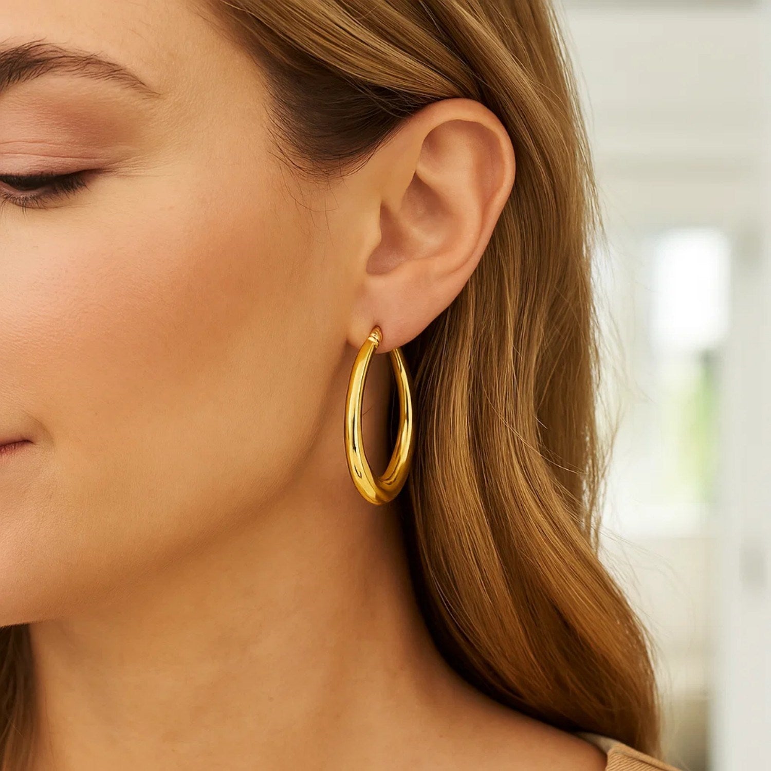 Oval electroform hoop earrings in 14K yellow gold on a woman's ear.