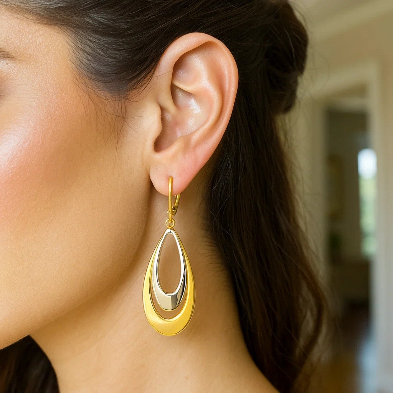 14k two-tone gold graduated open double teardrop earrings on a woman's ear.