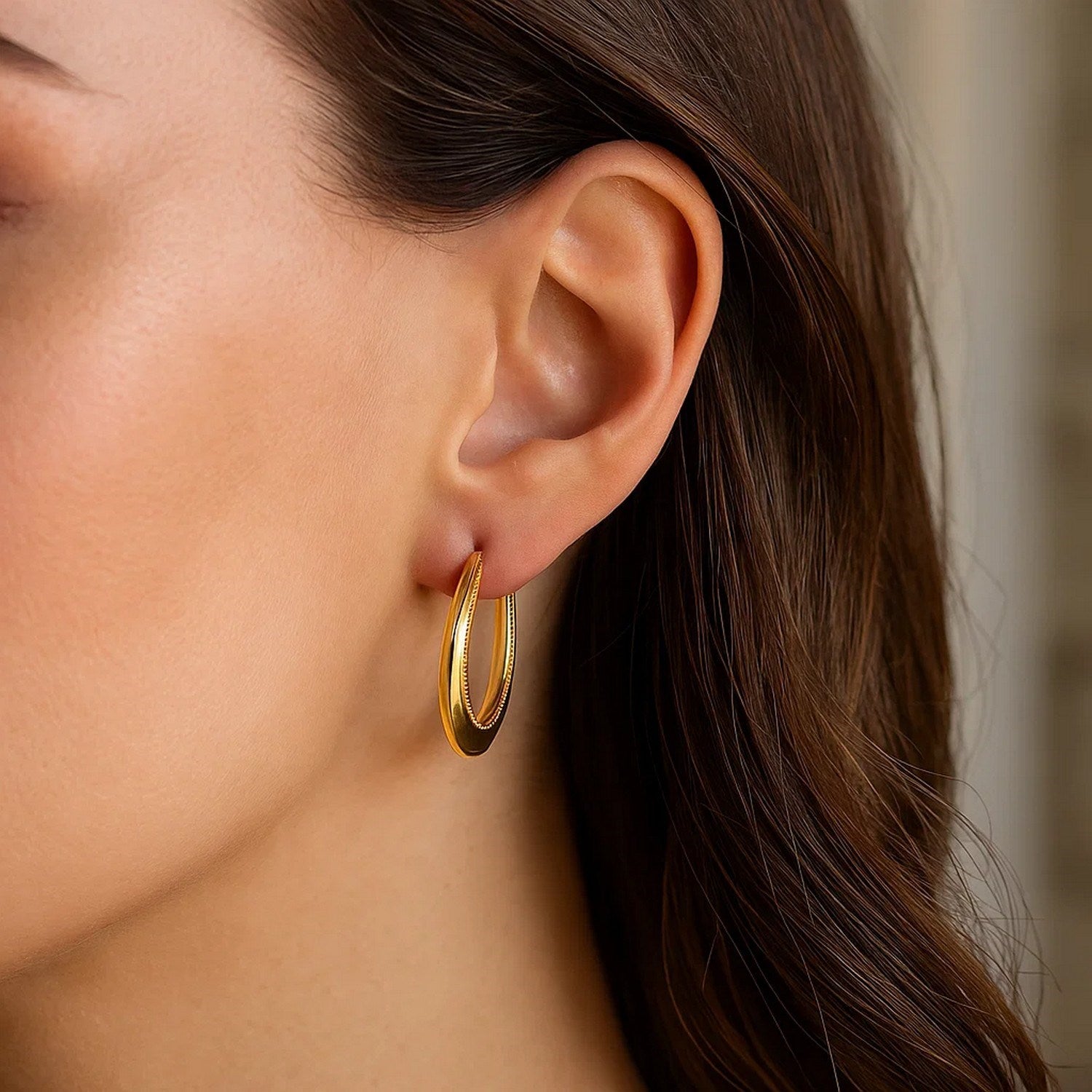 14k yellow gold round rope texture hoop earrings on a woman's ear.