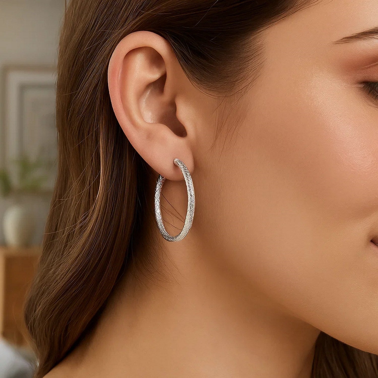 Sterling silver large hoop earrings with a braid texture are worn on an ear.